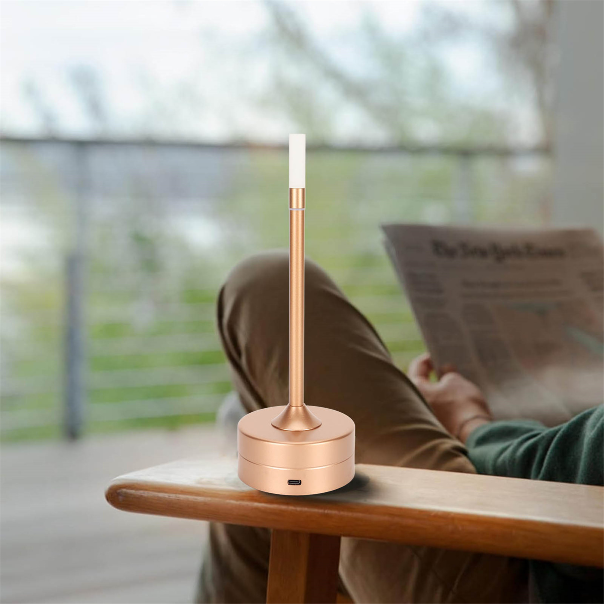 Person liest Zeitung mit goldfarbener Tischlampe auf einem hölzernen Beistelltisch. Hintergrund ist unscharf.