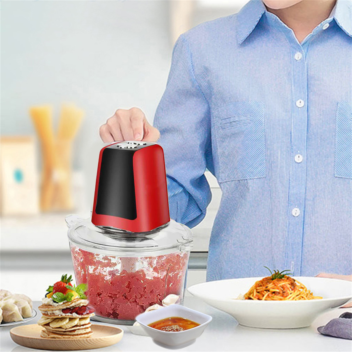 Eine Frau benutzt einen rot-schwarzen Küchenmixer. Auf dem Tisch werden zubereitete Speisen präsentiert: Pasta, Snacks und Soße.