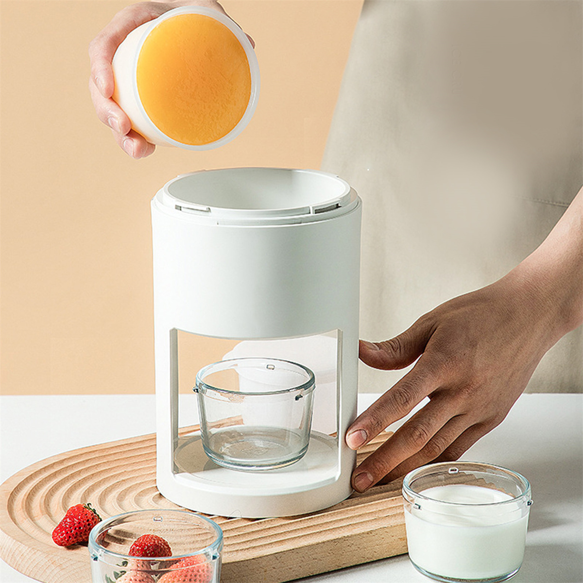 Eine Person platziert eine orangefarbene Kugel in eine weiße Maschine. Hintergrund: ein Holzbrett.