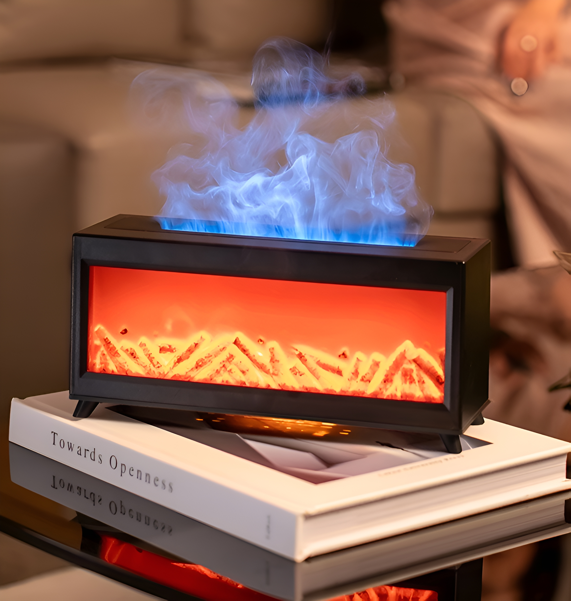 Ein dekorativer Kamin mit blauem Flammeneffekt, auf einem Buch, auf einem Glastisch.
