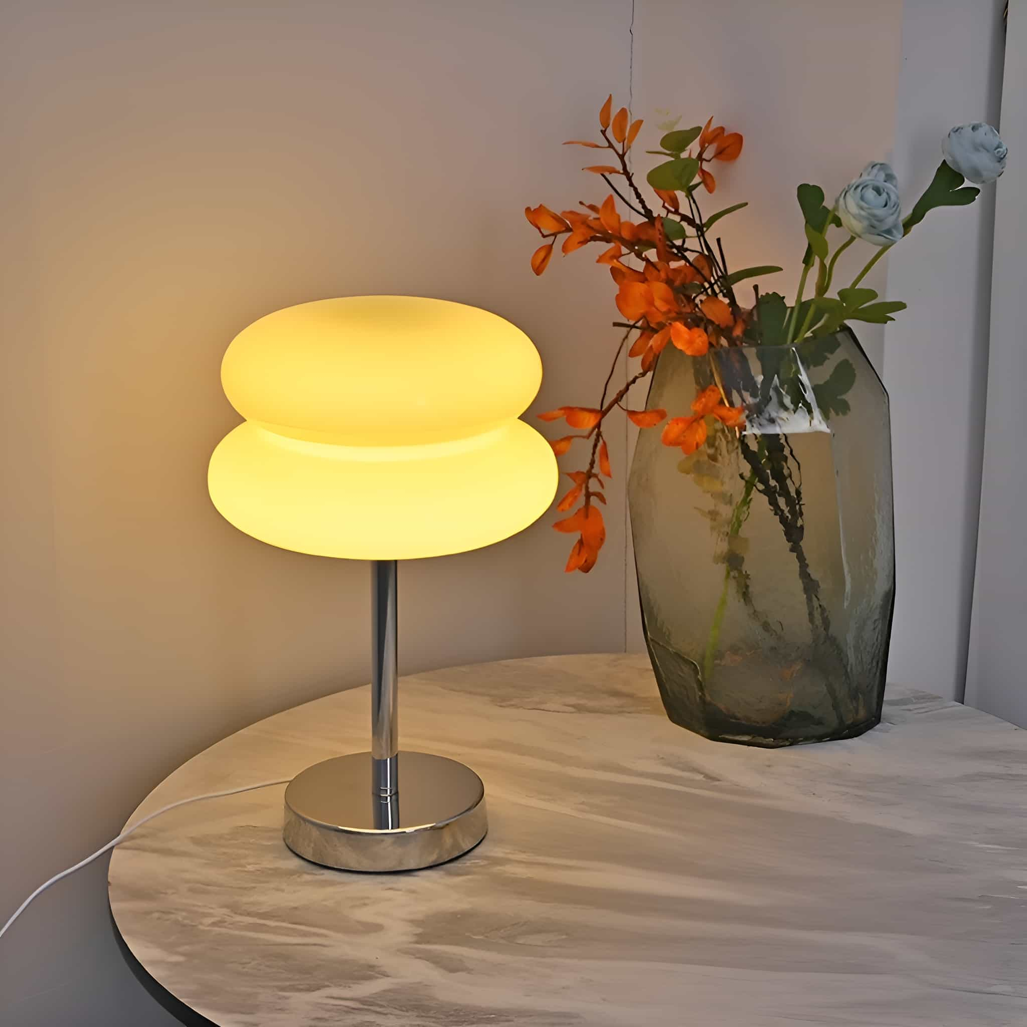 Eine Tischlampe mit einem doppellagigen gelben Schirm, neben einer Vase mit orangefarbenen und blauen Blumen.