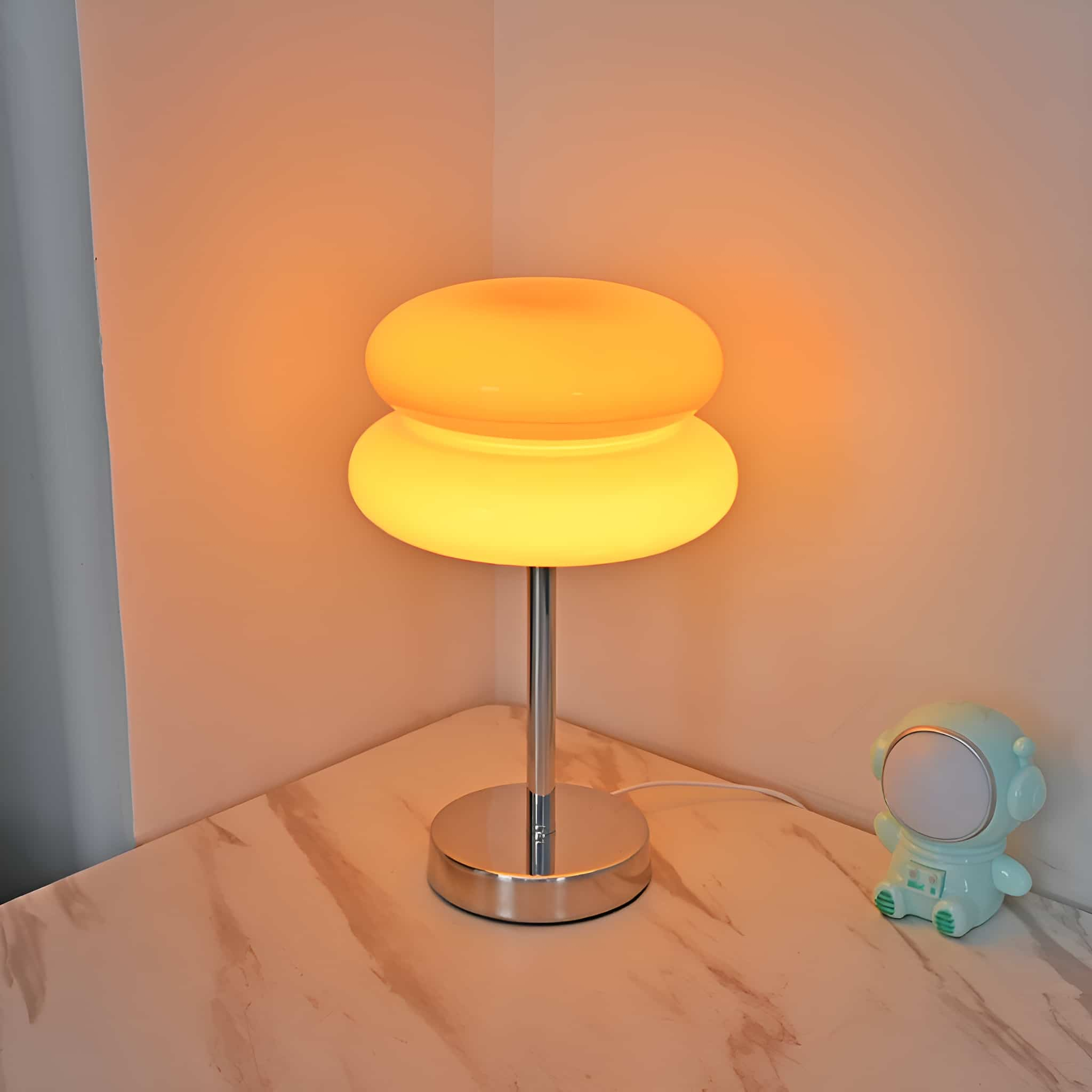 Eine Lampe mit rundem Ober- und Unterteil in Form einer Acht, auf einem Tisch neben einem Spielzeug-Astronauten.