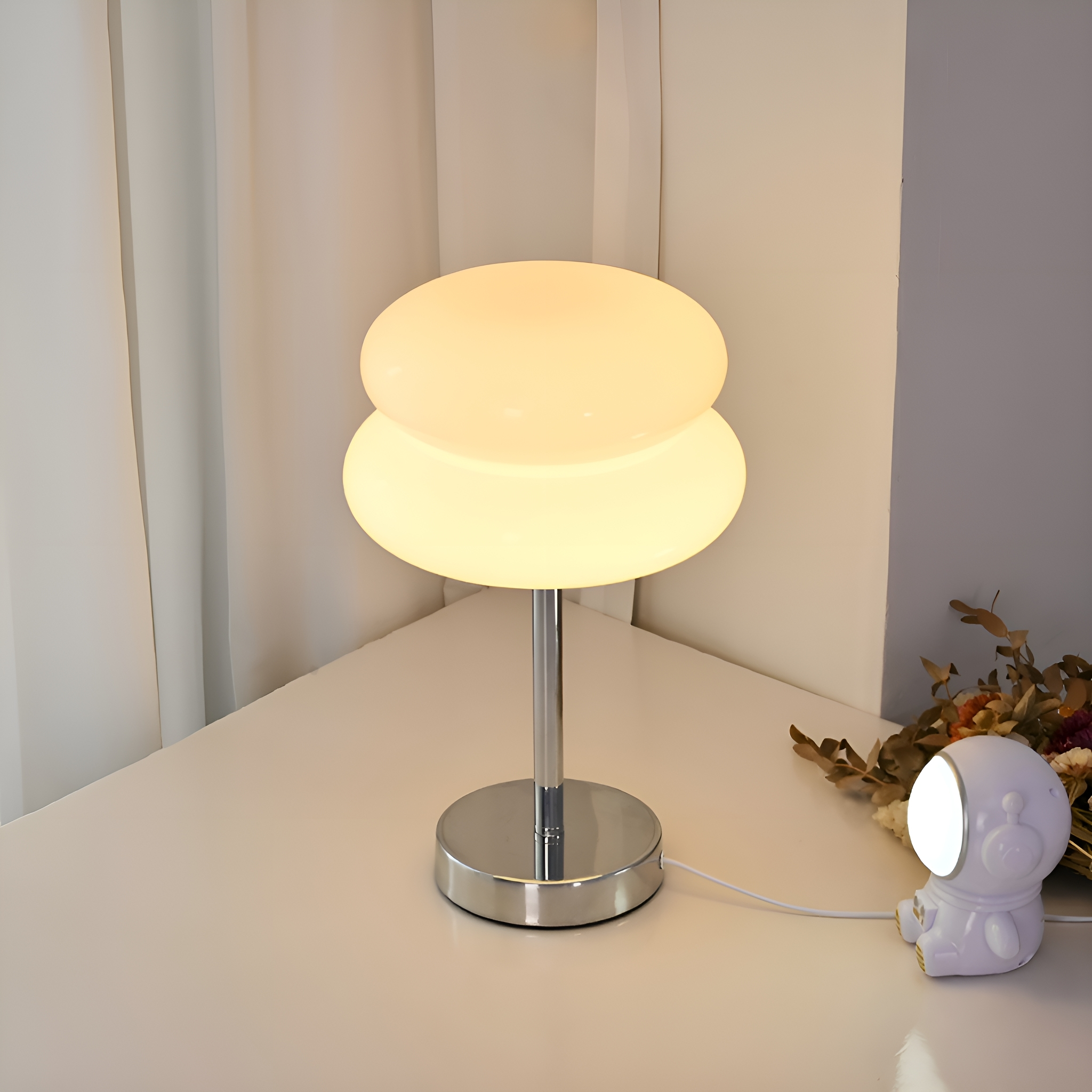 Moderne weiße Lampe mit zwei übereinanderliegenden ovalen Schirmen auf weißem Tisch.