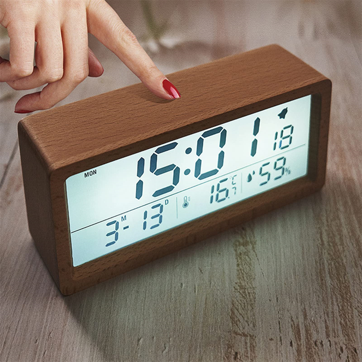 Eine hölzerne Digitaluhr zeigt Zeit, Datum, Temperatur und Luftfeuchtigkeit an. Ein Finger berührt den Bildschirm.