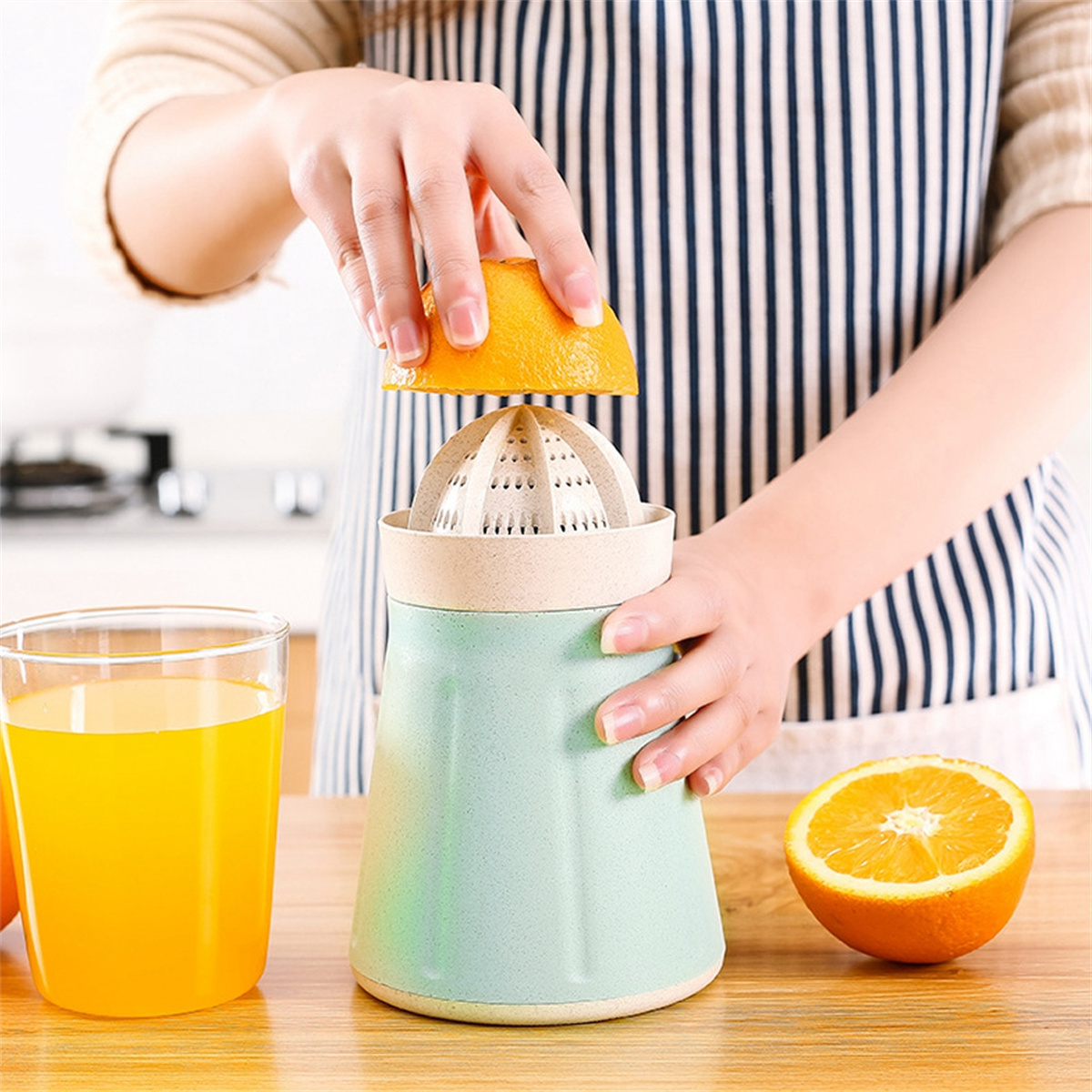 Person quetscht Orange mit manueller Saftpresse. Glas Saft und halbe Orange sichtbar.