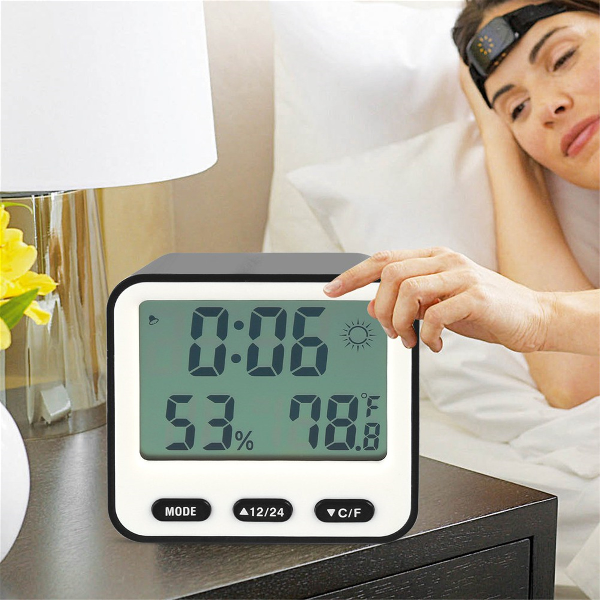 Eine Digitaluhr zeigt die Uhrzeit, Temperatur und Luftfeuchtigkeit an. Eine Frau schläft im Bett.