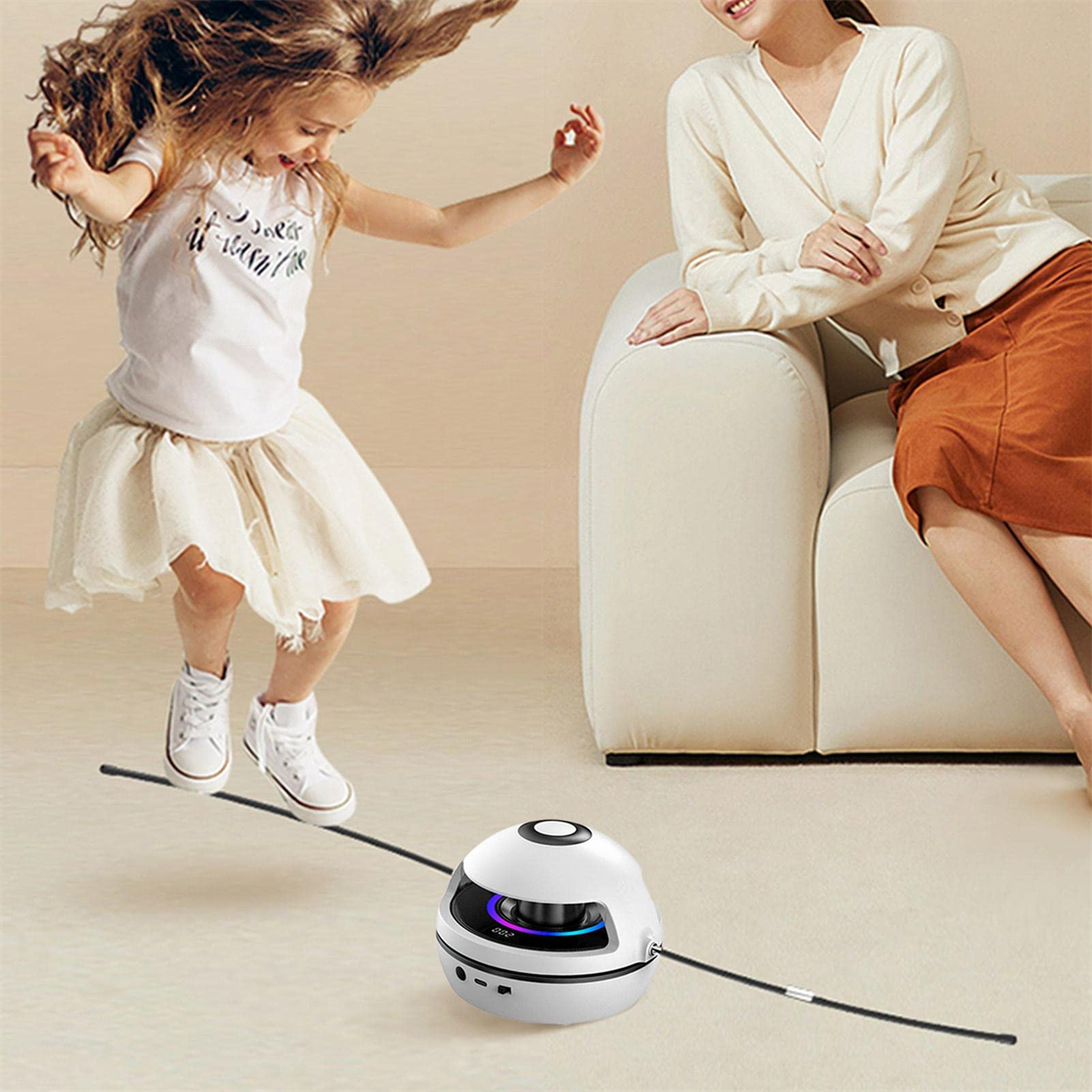 Ein kleines Mädchen springt über ein weißes Roboter-Spielzeug, an dem ein schwarzes Seil befestigt ist. Eine Frau schaut zu.