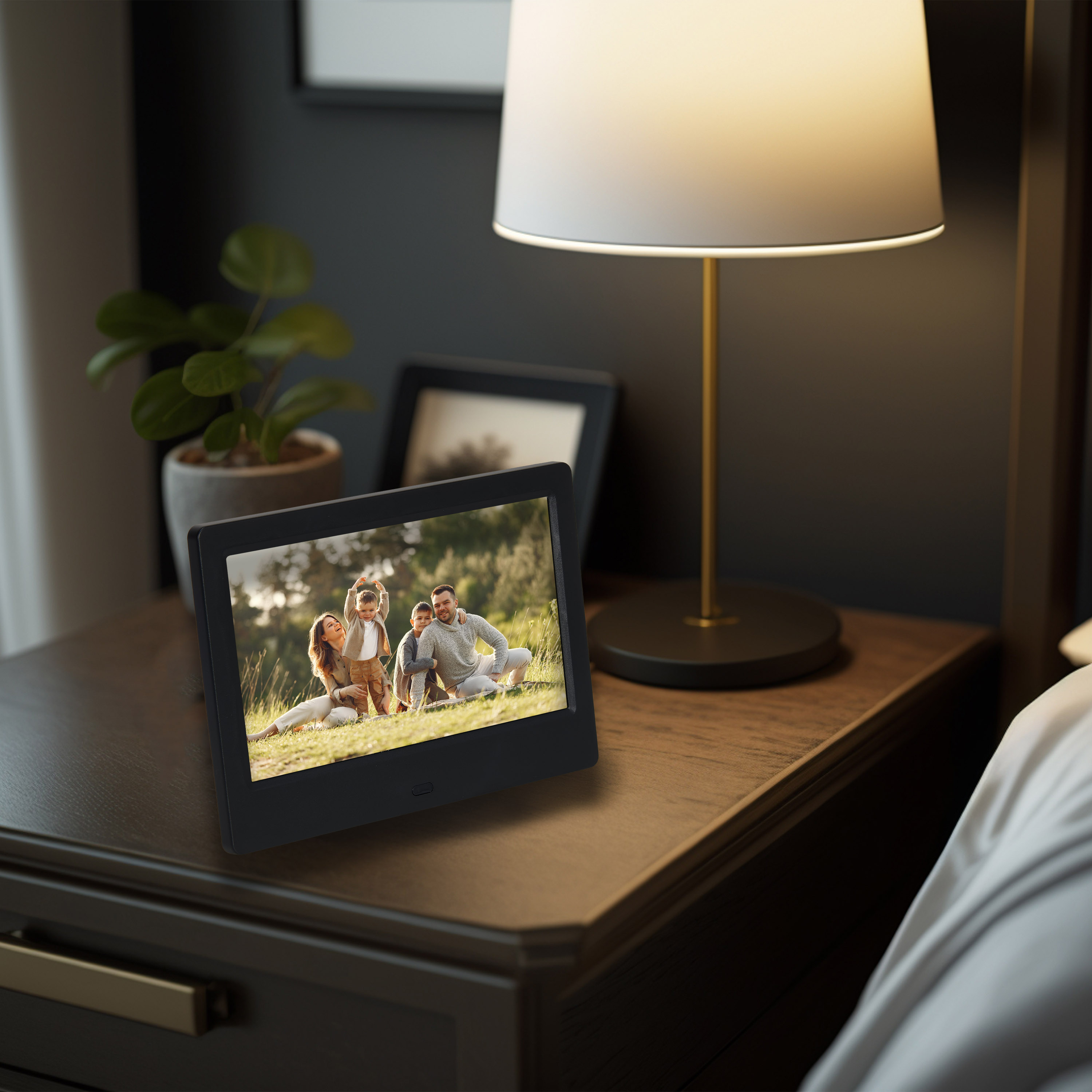 Digitale fotolijst op een nachtkastje met een familiefoto, met een lamp op de achtergrond.