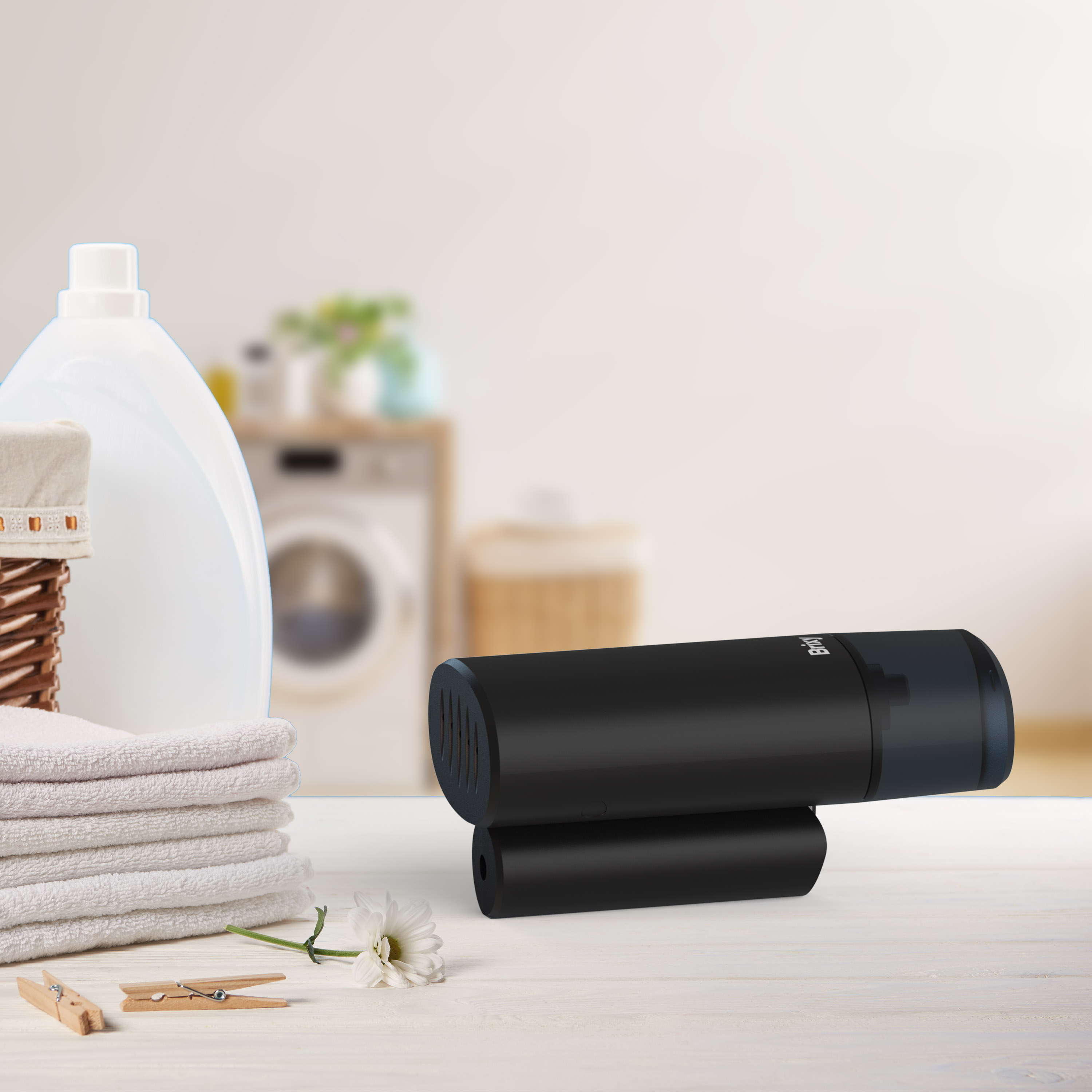 A black device with a small tube attached, sitting on a table. A laundry scene is in background.