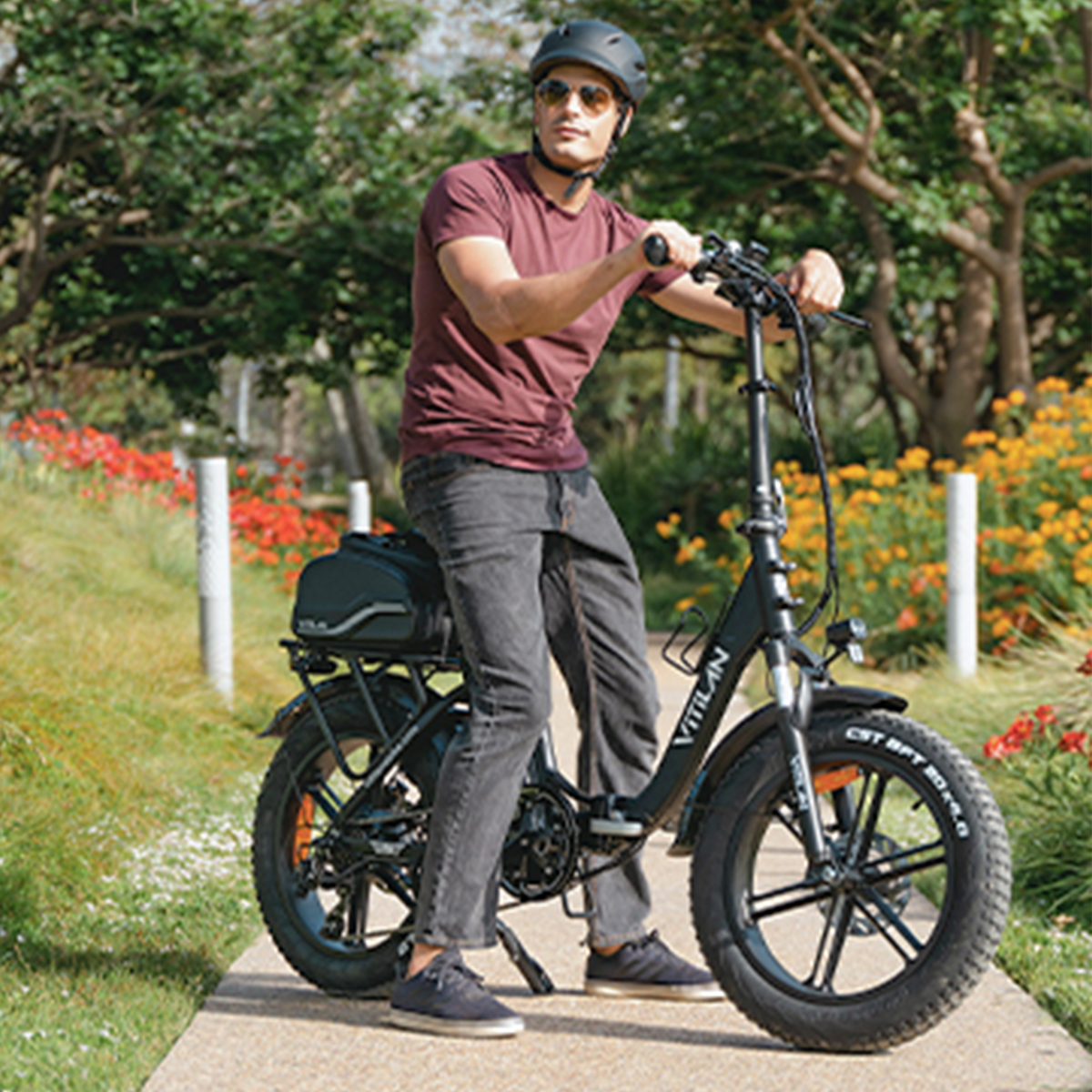 Mężczyzna w kasku jedzie czarnym składanym rowerem elektrycznym po utwardzonej ścieżce.