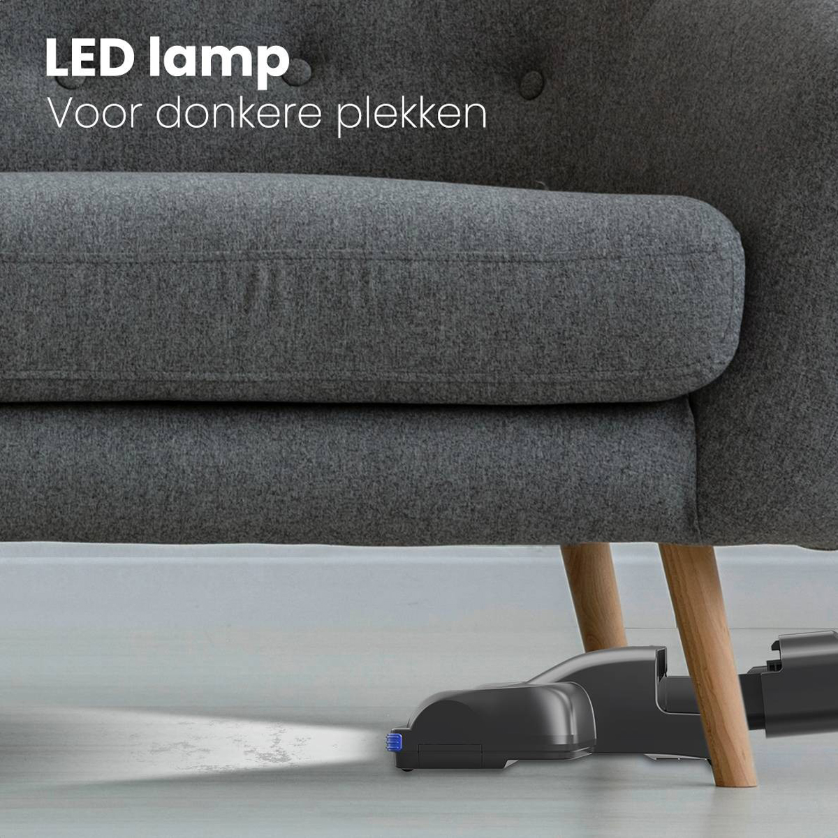 Vacuum cleaner nozzle under a gray sofa, with a light shining on the floor.