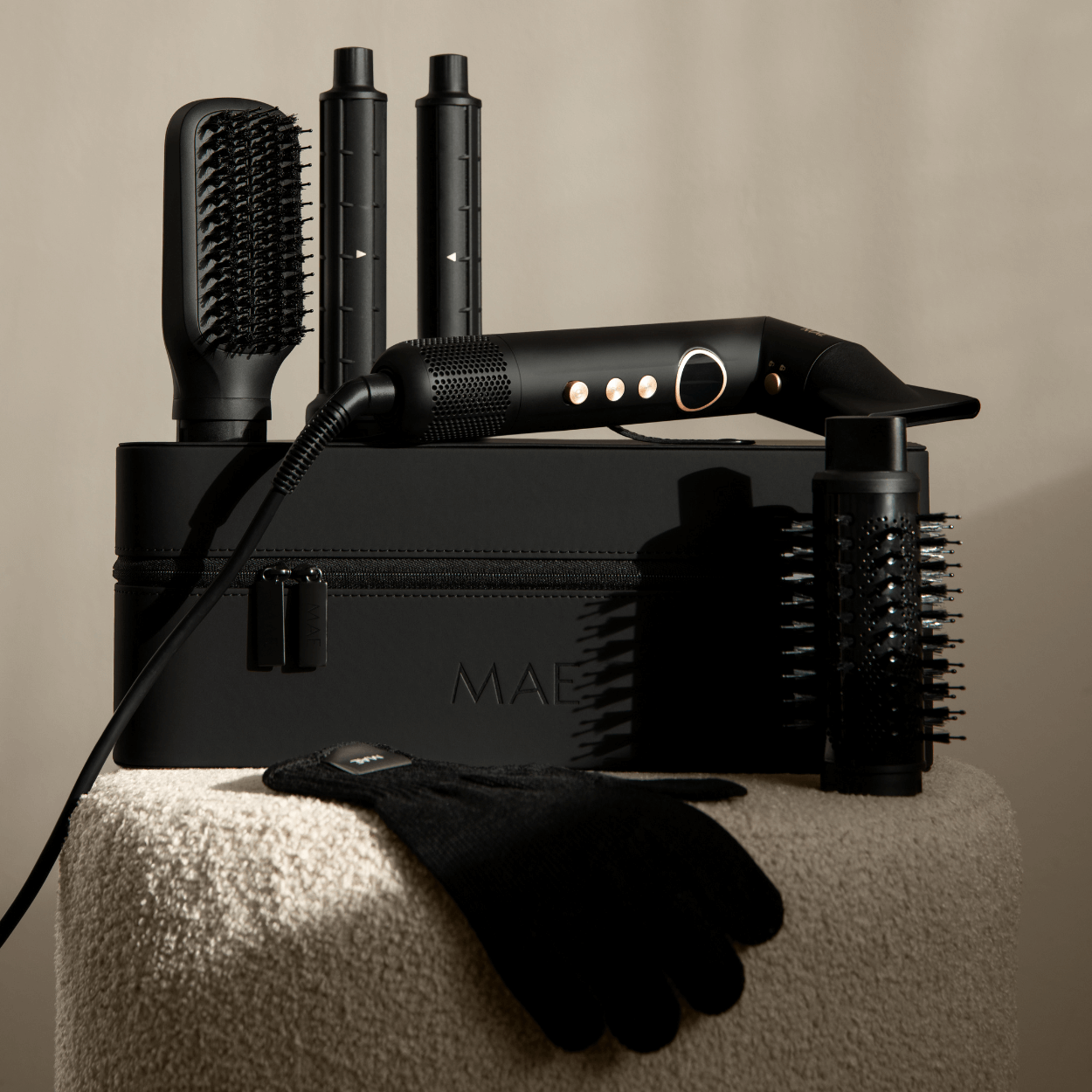 Black hair styling set with a hairdryer, brush, and other attachments on a stool.
