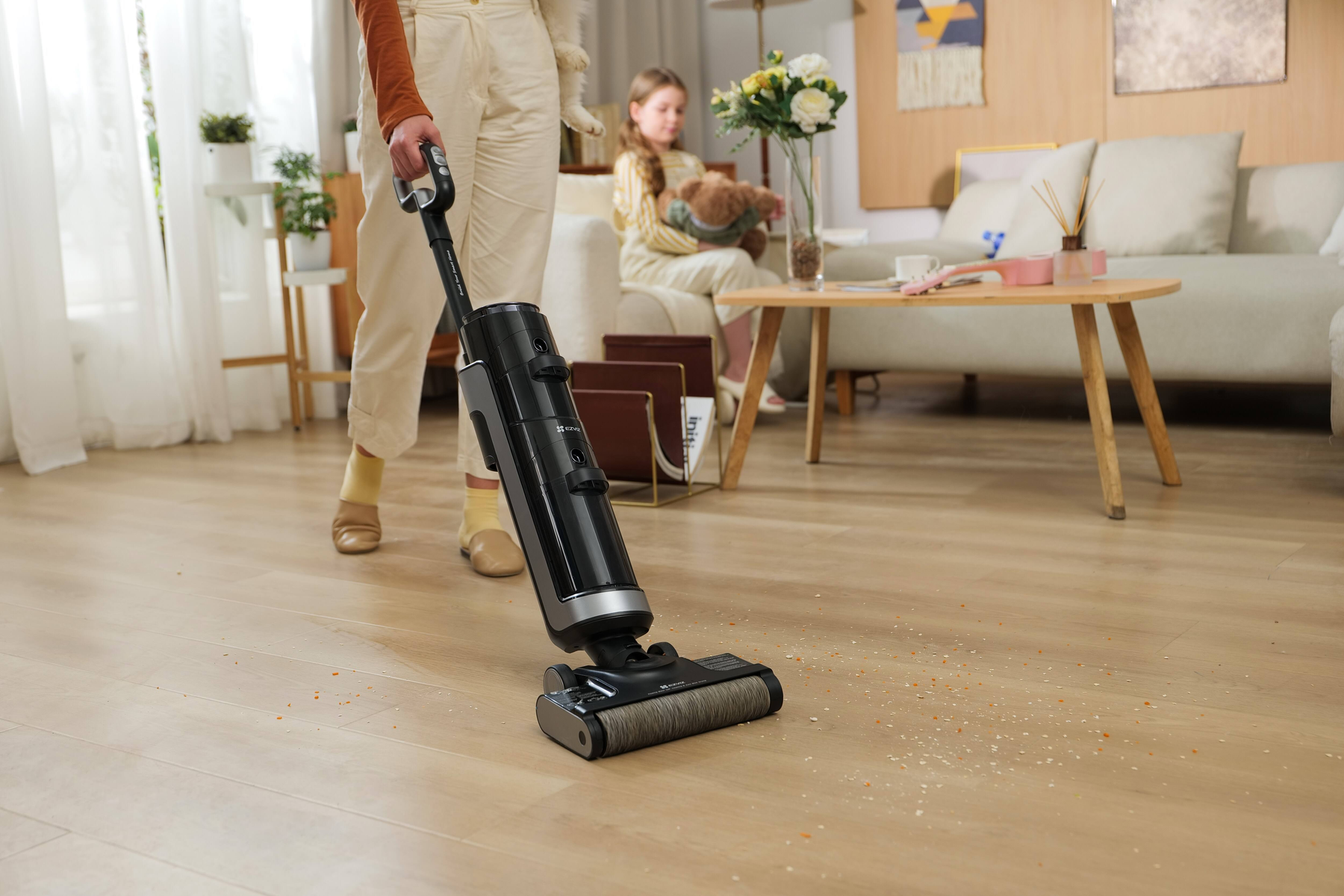 Persona che aspira il pavimento in legno con un aspirapolvere nero senza fili.
