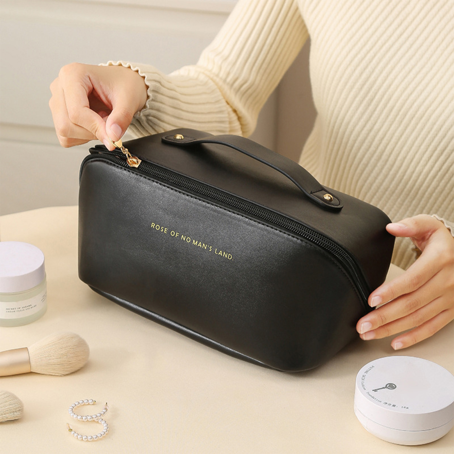 Eine schwarze Make-up-Tasche mit goldfarbenen Buchstaben, die von einer Person zugezogen wird.