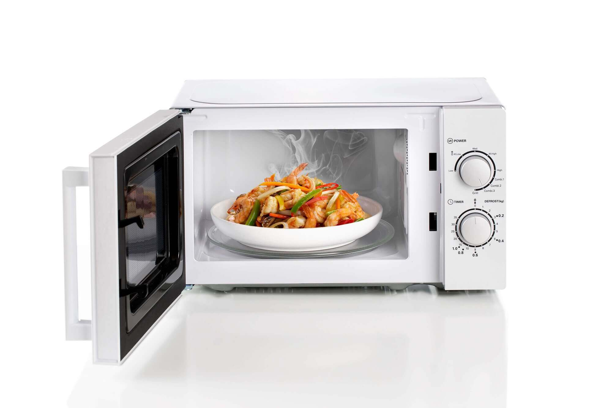 Witte magnetron met eten erin, deur open. Een bord met eten is zichtbaar, de bediening is rechts.