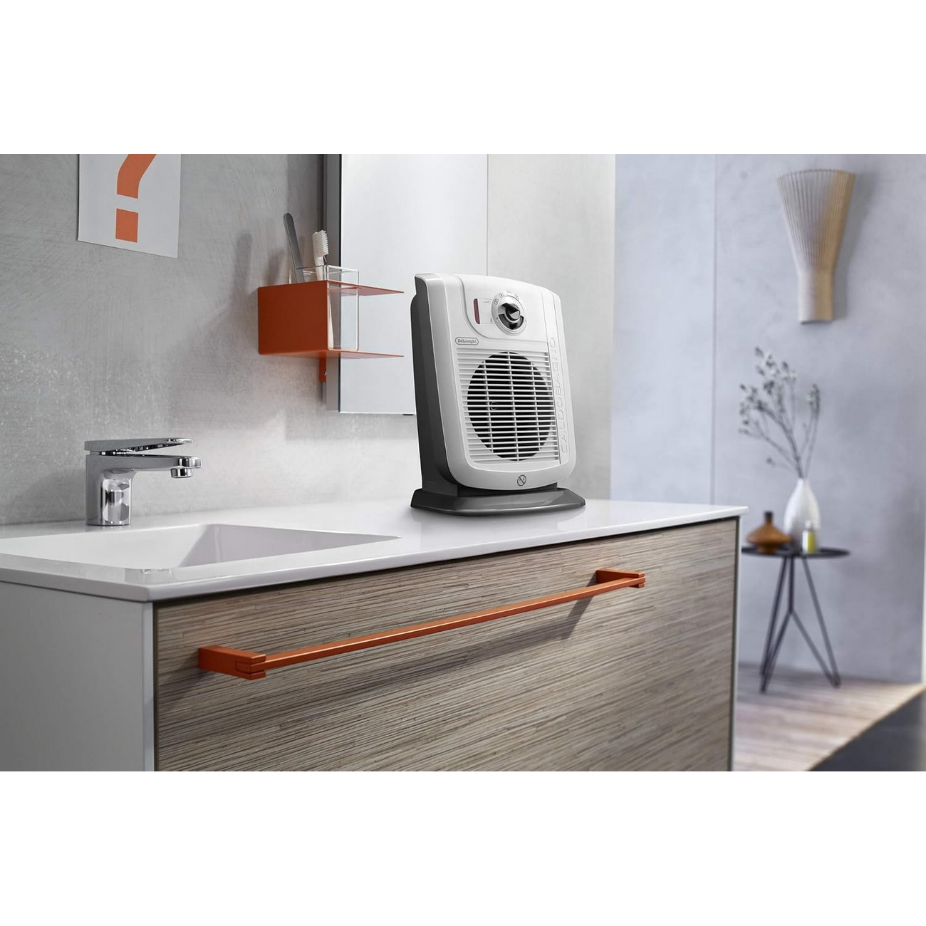 Łazienka z białym i szarym grzejnikiem wentylatorowym na blacie. Widoczne lustro i pomarańczowa półka.