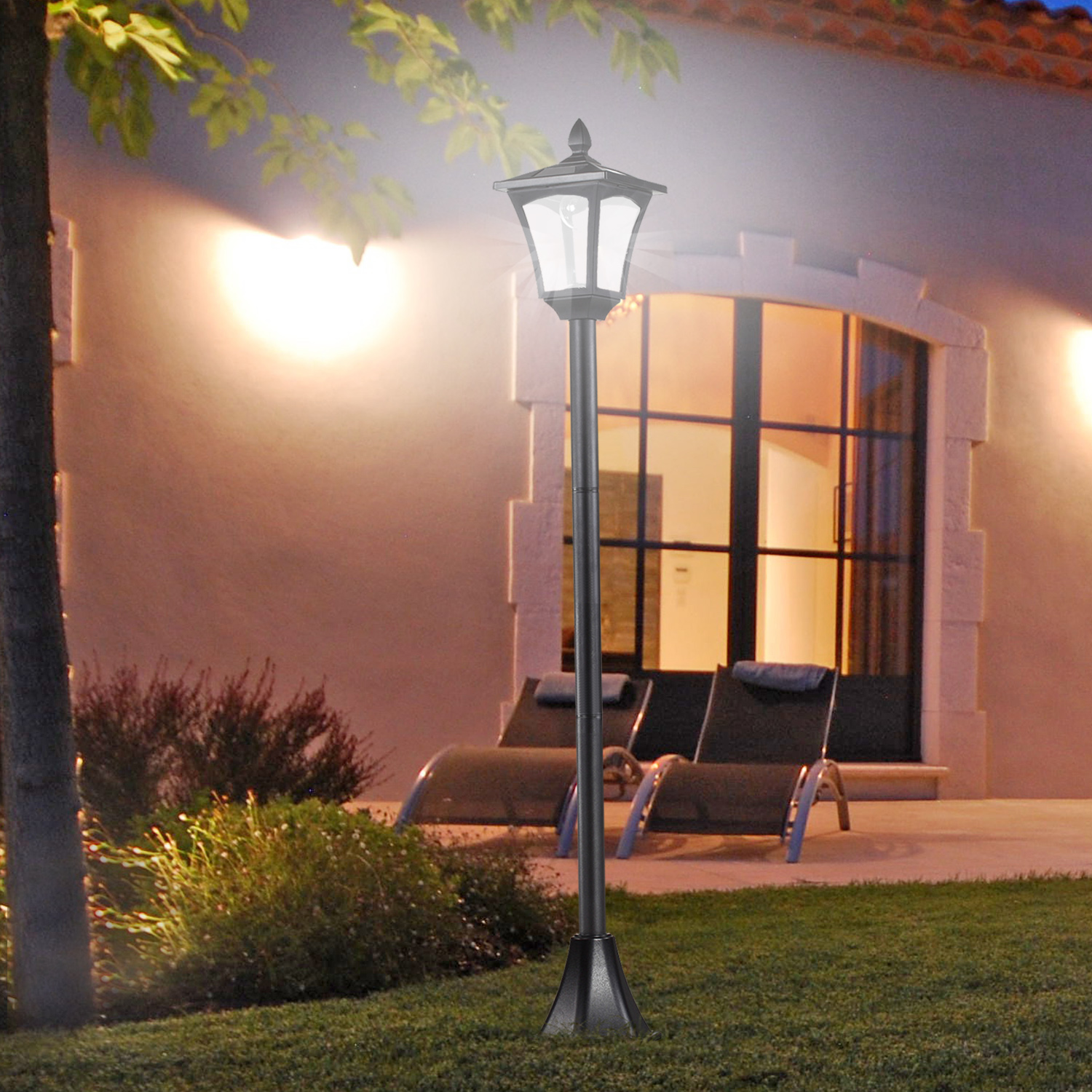 Lampione da giardino con luce accesa, che illumina un patio con sedie e una casa sullo sfondo.