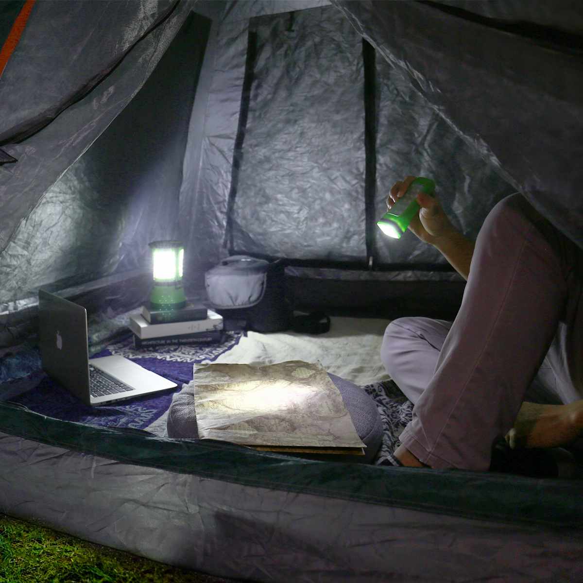 In einem Zelt hält eine Person eine Taschenlampe und betrachtet eine Karte auf einer Decke.
