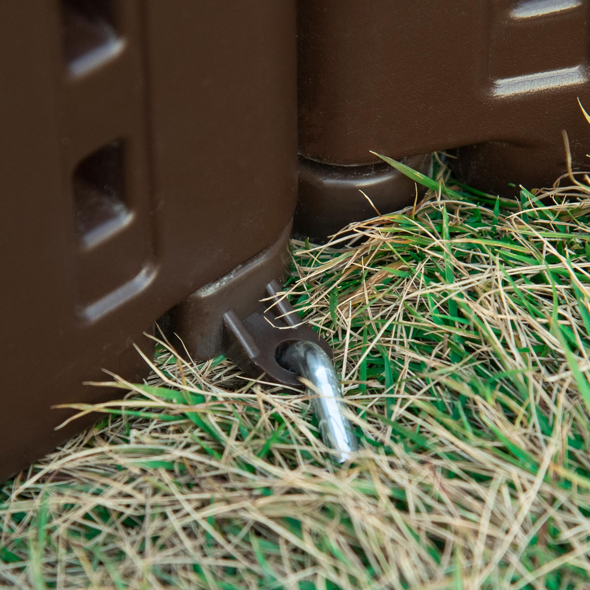 Un bidone per il compost marrone nell'erba. È visibile una cerniera metallica. L'area è all'aperto.