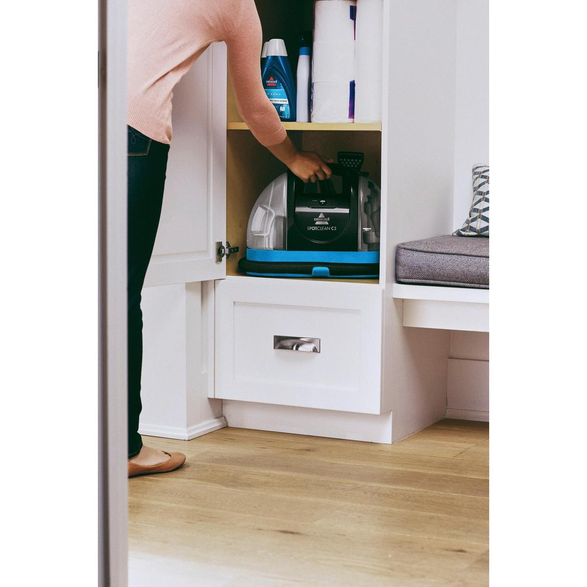 Bir kişi, bir Bissell SpotClean C3 temizleyiciyi ortaya çıkarmak için beyaz bir dolap açıyor.