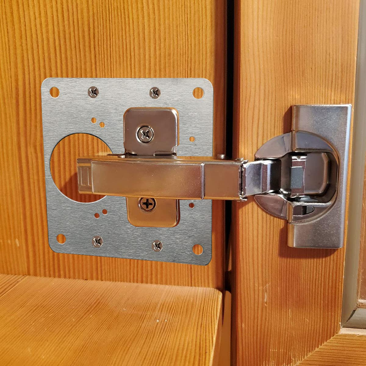 Una cerniera argentata montata su una porta di legno. La cerniera è cromata.