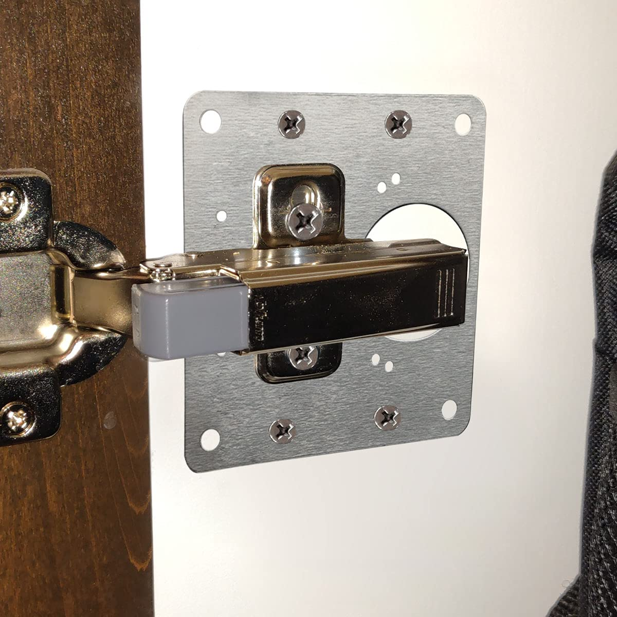 Una cerniera per anta di armadio argentata fissata a una porta bianca e un telaio marrone.