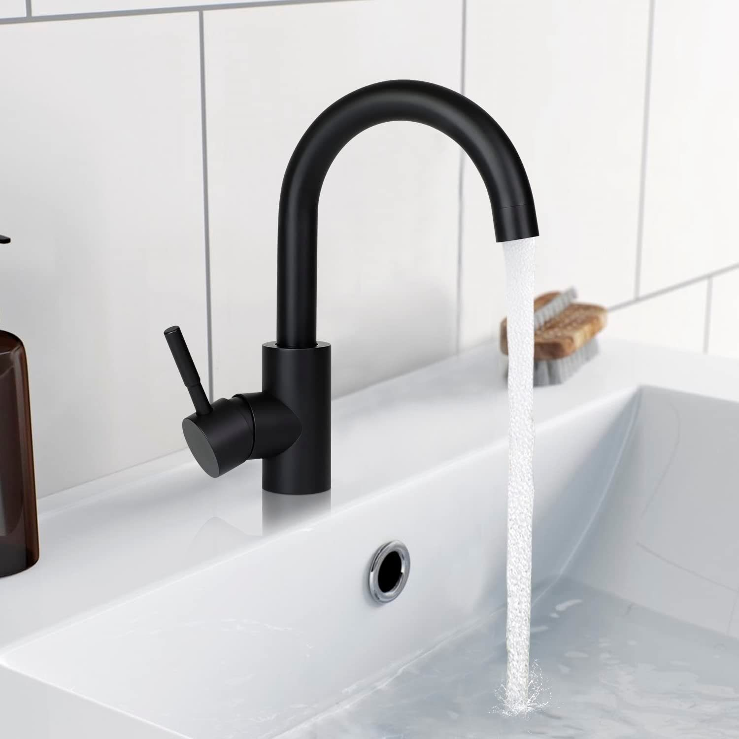 Schwarze Armatur mit fließendem Wasser in einem weißen Waschbecken. Seifenspender und Bürste sichtbar.