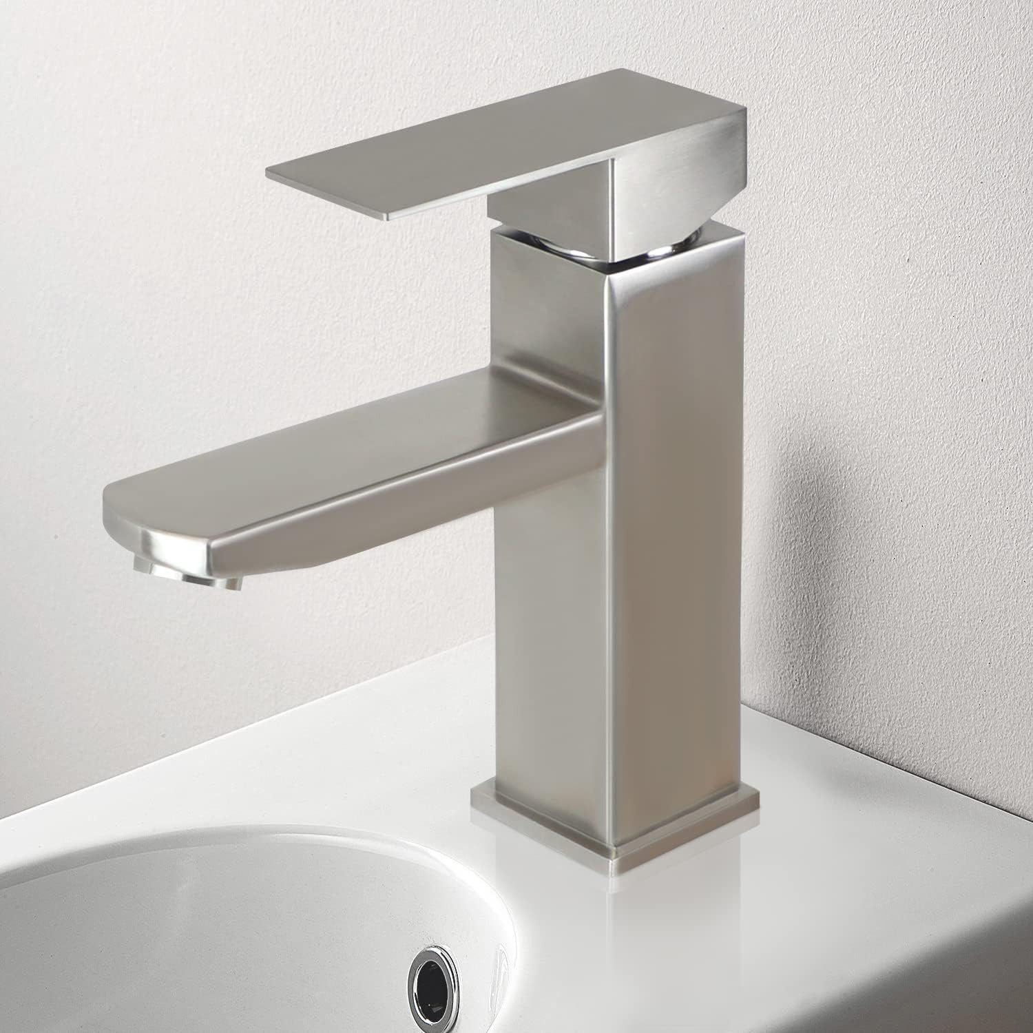 Ein Wasserhahn aus Edelstahl mit quadratischem Design, auf einem weißen Waschbecken. Es ist ein minimalistisches Design.