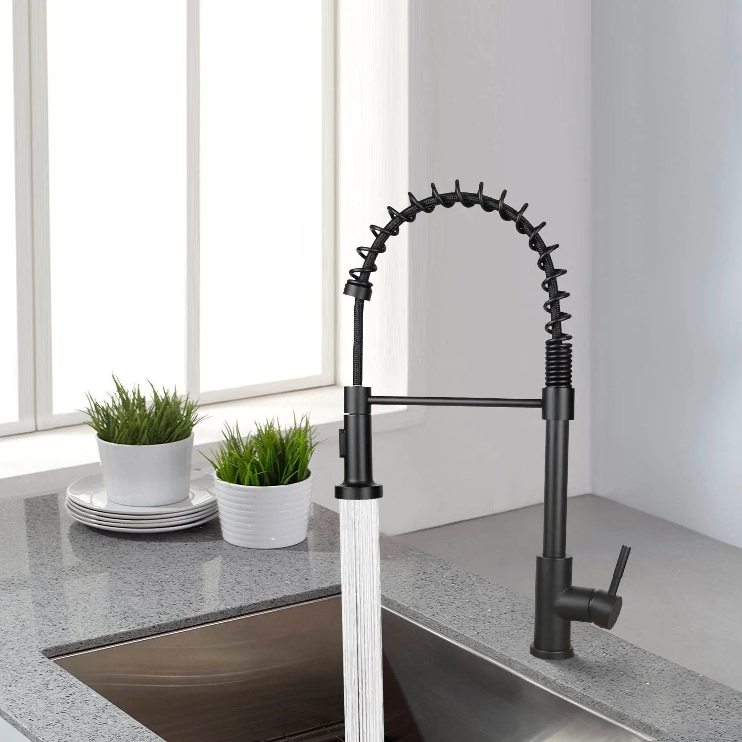 Ein schwarzer Küchenhahn mit flexibler Feder, sprühendes Wasser, auf einer grauen Arbeitsplatte.