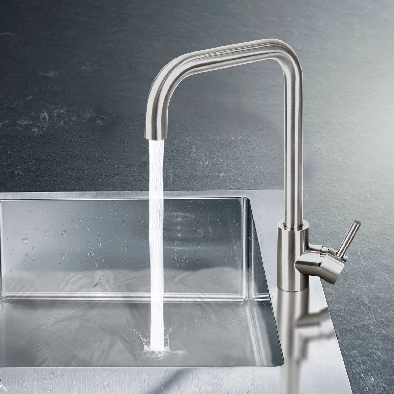 Un rubinetto da cucina argentato con acqua che scorre in un lavello in acciaio inossidabile, su un piano di lavoro scuro.