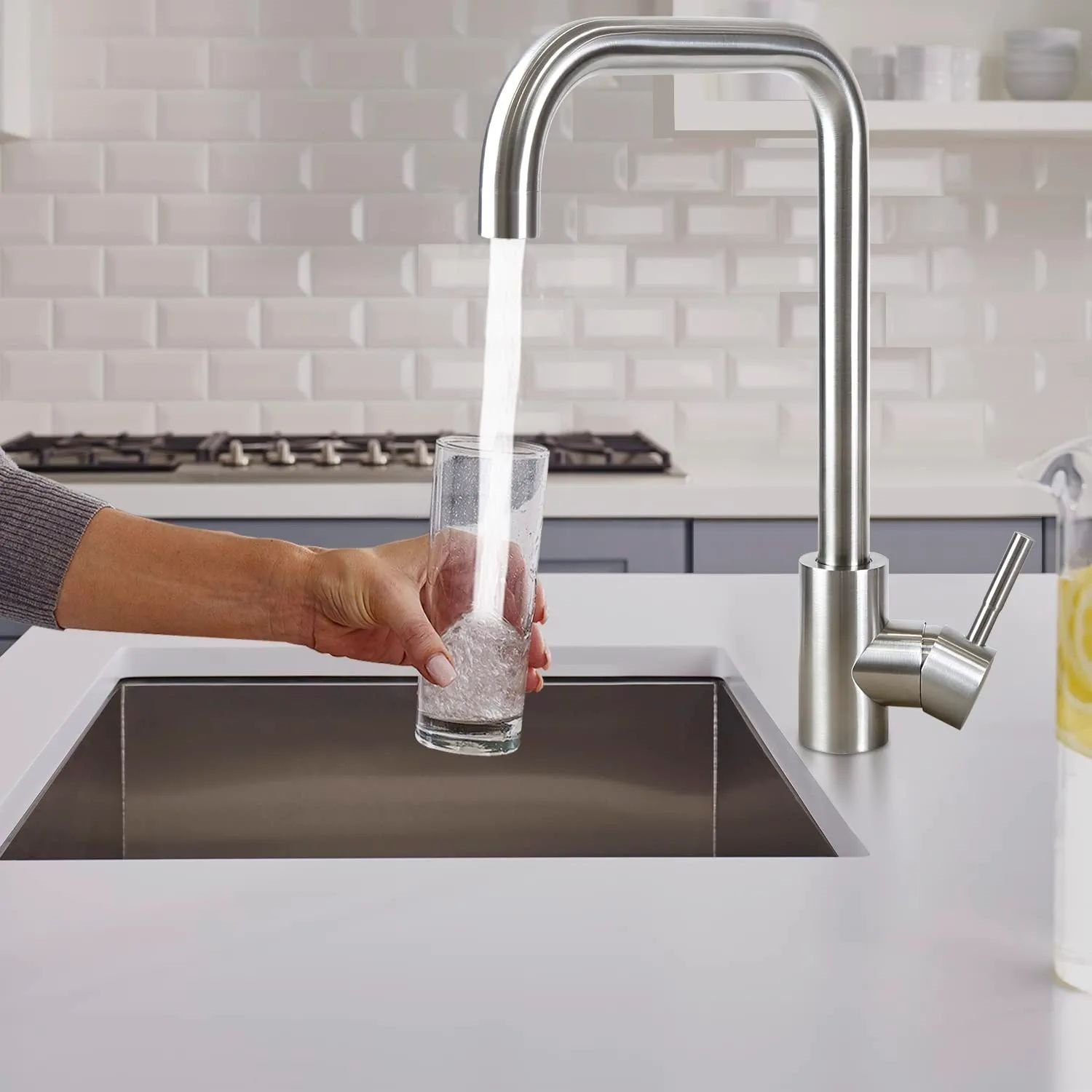 Un rubinetto da cucina con acqua corrente che riempie un bicchiere in un lavandino bianco.