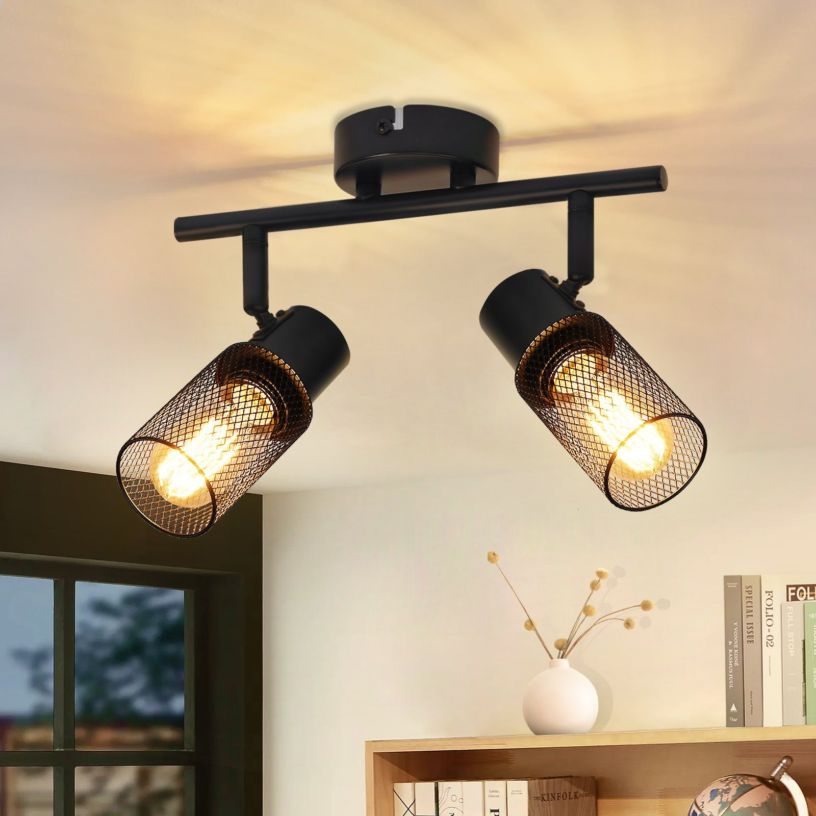 Due lampade a faretto nere su un soffitto, con luce calda e alcuni oggetti sullo sfondo.