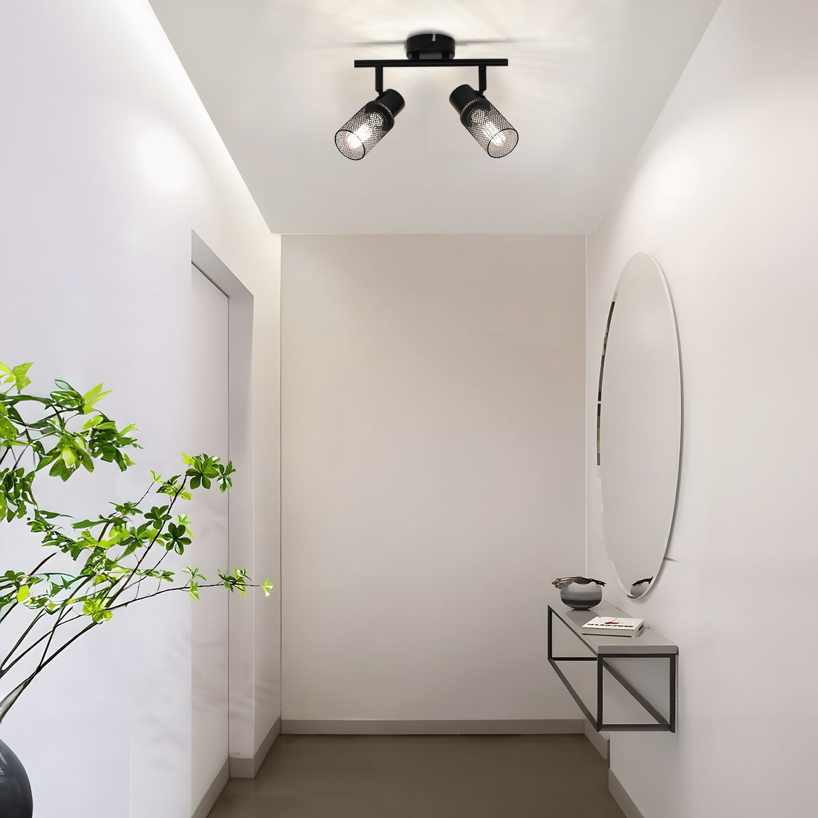 Un corridoio con due faretti neri sul soffitto, uno specchio e una consolle.