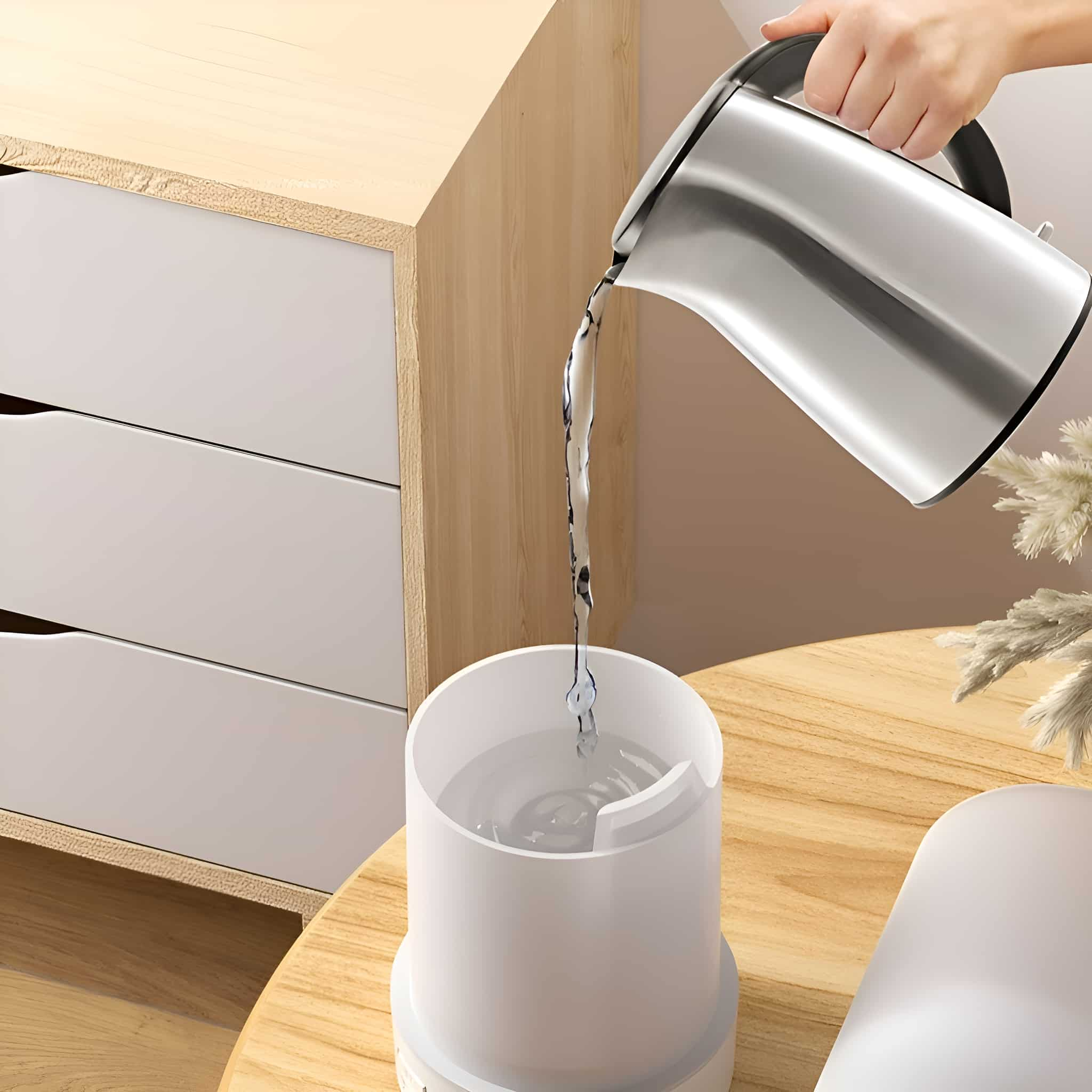 Eine Person gießt Wasser aus einem silbernen Wasserkocher in einen weißen Luftbefeuchter.