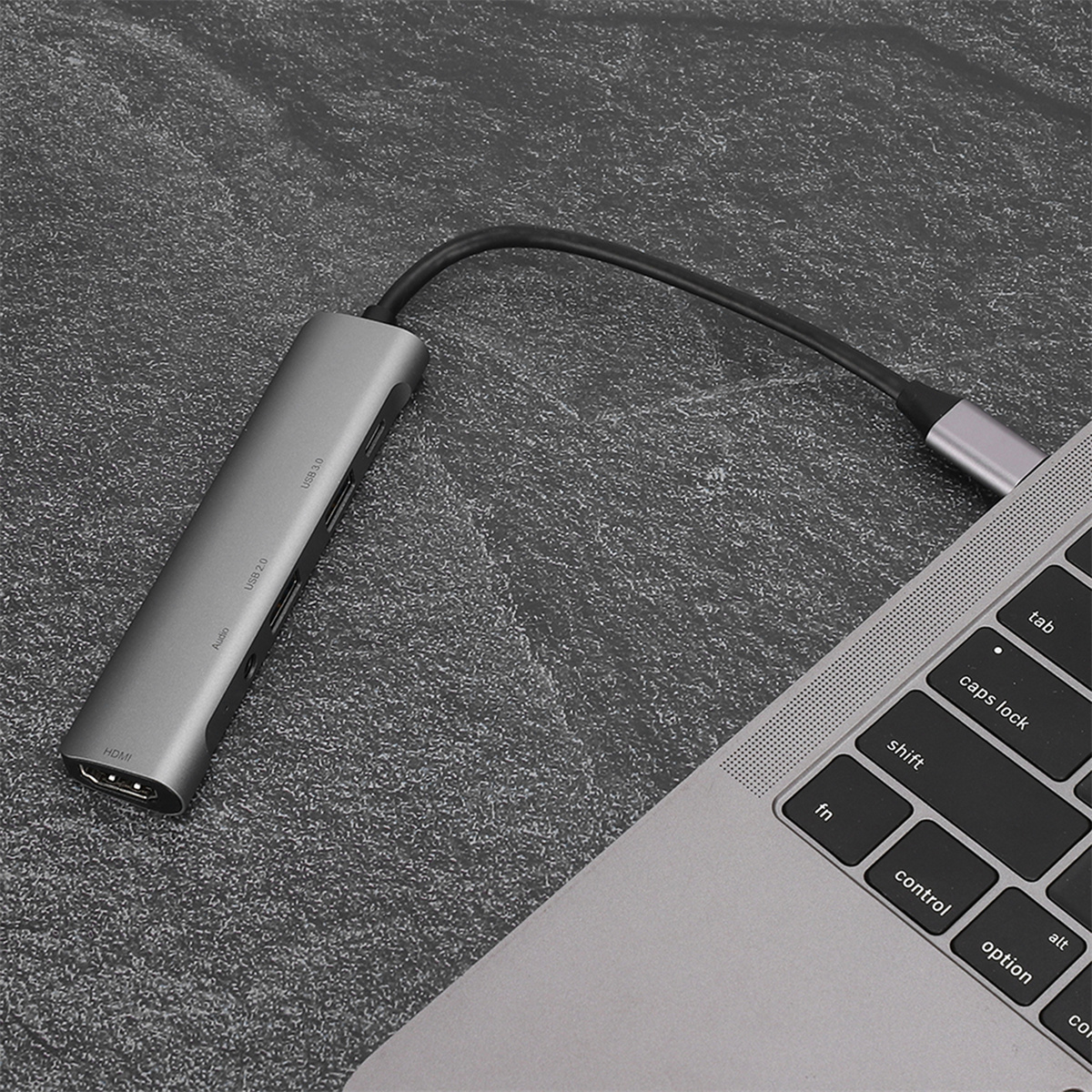 Laptop und ein grauer USB-Hub mit mehreren Anschlüssen auf strukturierter Oberfläche.