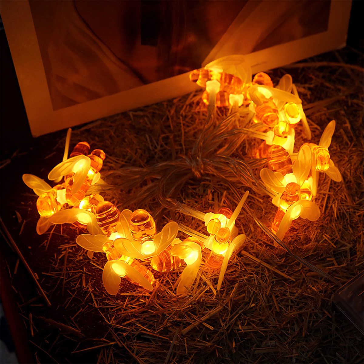 Lichterkette in Bienenform, gelb leuchtend, auf brauner Oberfläche, dunkler Hintergrund.