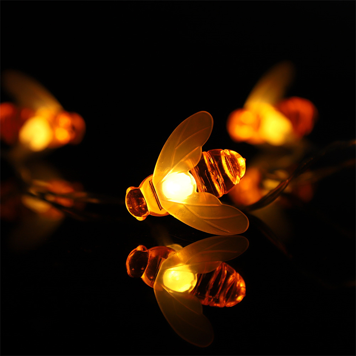 Eine Lichterkette in Bienenform. Die Bienen sind gelb und beleuchtet und spiegeln sich auf der dunklen Oberfläche.