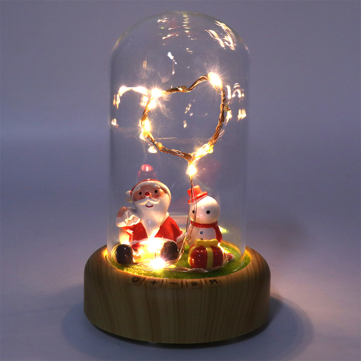 Weihnachtsdekoration in einer Glaskuppel mit Weihnachtsmann, Schneemann und Lichterkette auf Holzsockel.