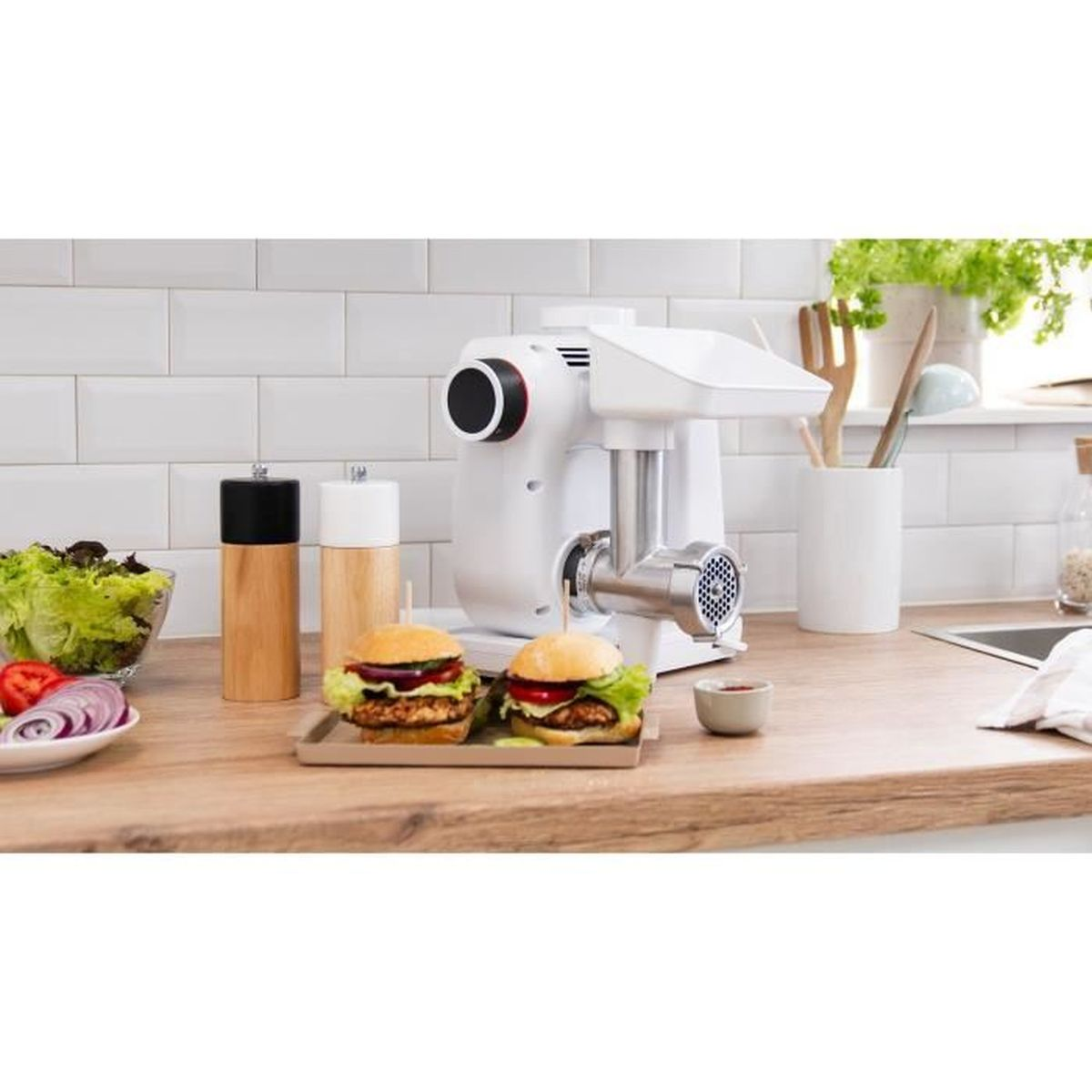 Eine weiße Küchenmaschine mit zwei Hamburgern und Zutaten auf einer Holzoberfläche, weißer Fliesenhintergrund.