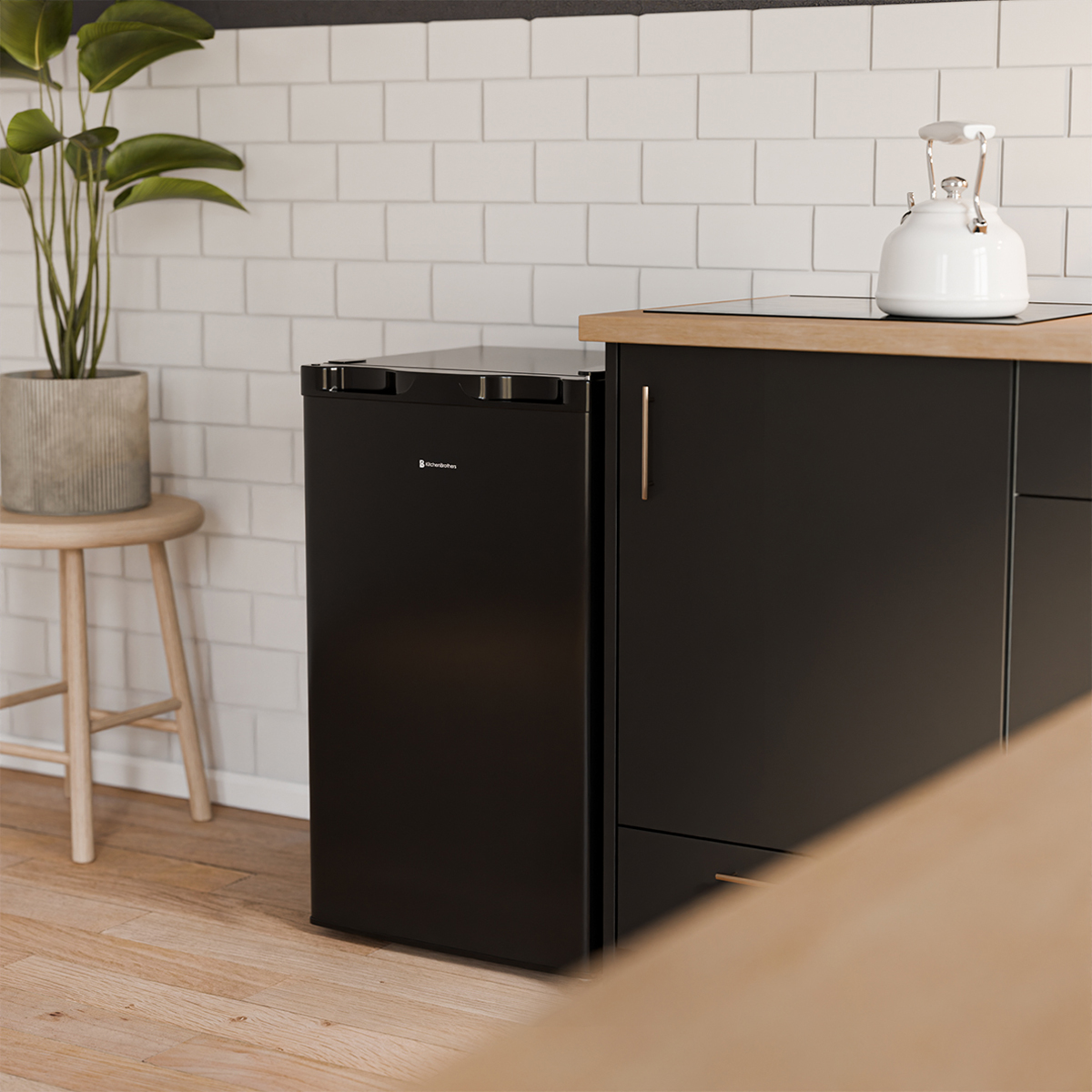 Un mini-réfrigérateur noir à côté d'un meuble en bois et d'un tabouret avec une plante.