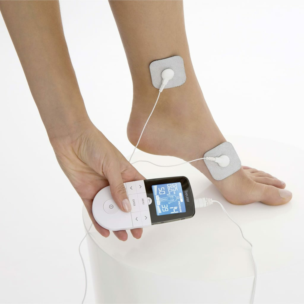 Eine Person, die ein Elektrotherapiegerät an ihrem Fuß verwendet, mit angebrachten Pads.