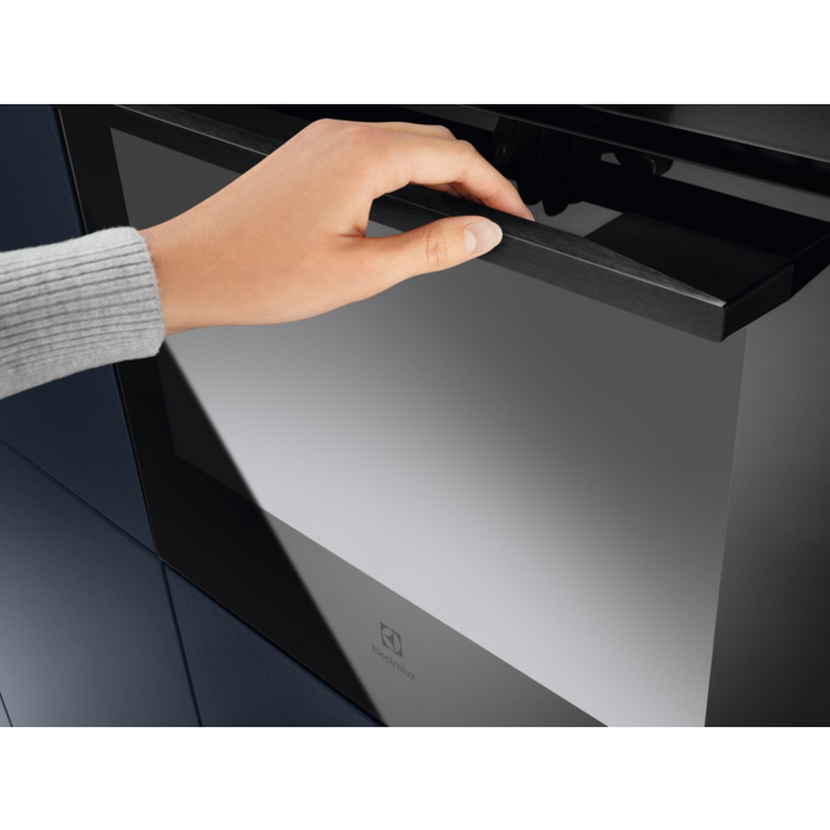 Una mano che apre una porta del forno nera. Il forno e i mobili circostanti sono blu scuro.