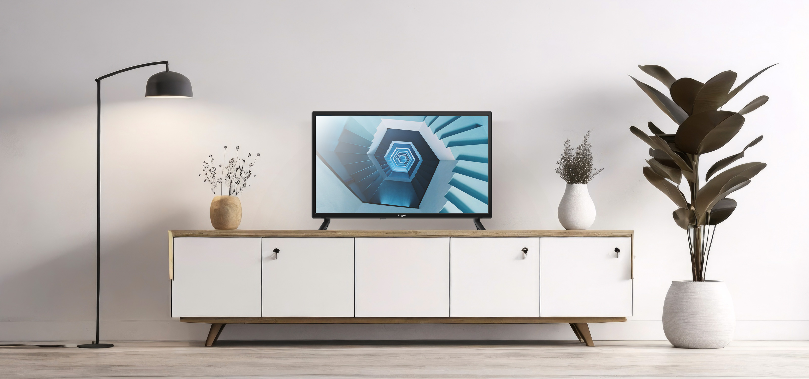 Salon z telewizorem, lampą podłogową, białą szafką i dużą rośliną.