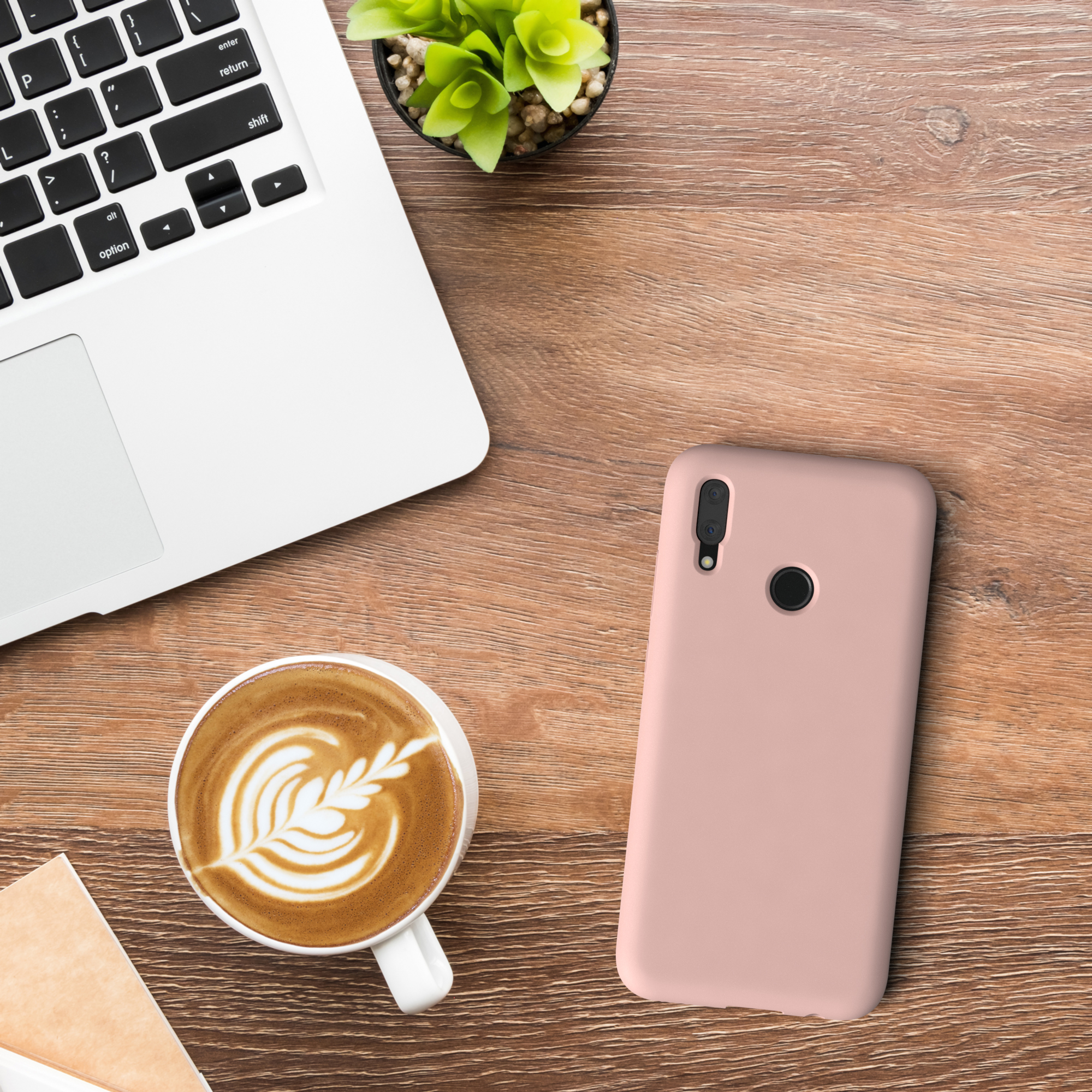 Ein Schreibtisch mit Laptop, Kaffeetasse, Telefon und Pflanze. Das Telefon hat eine rosa Hülle.