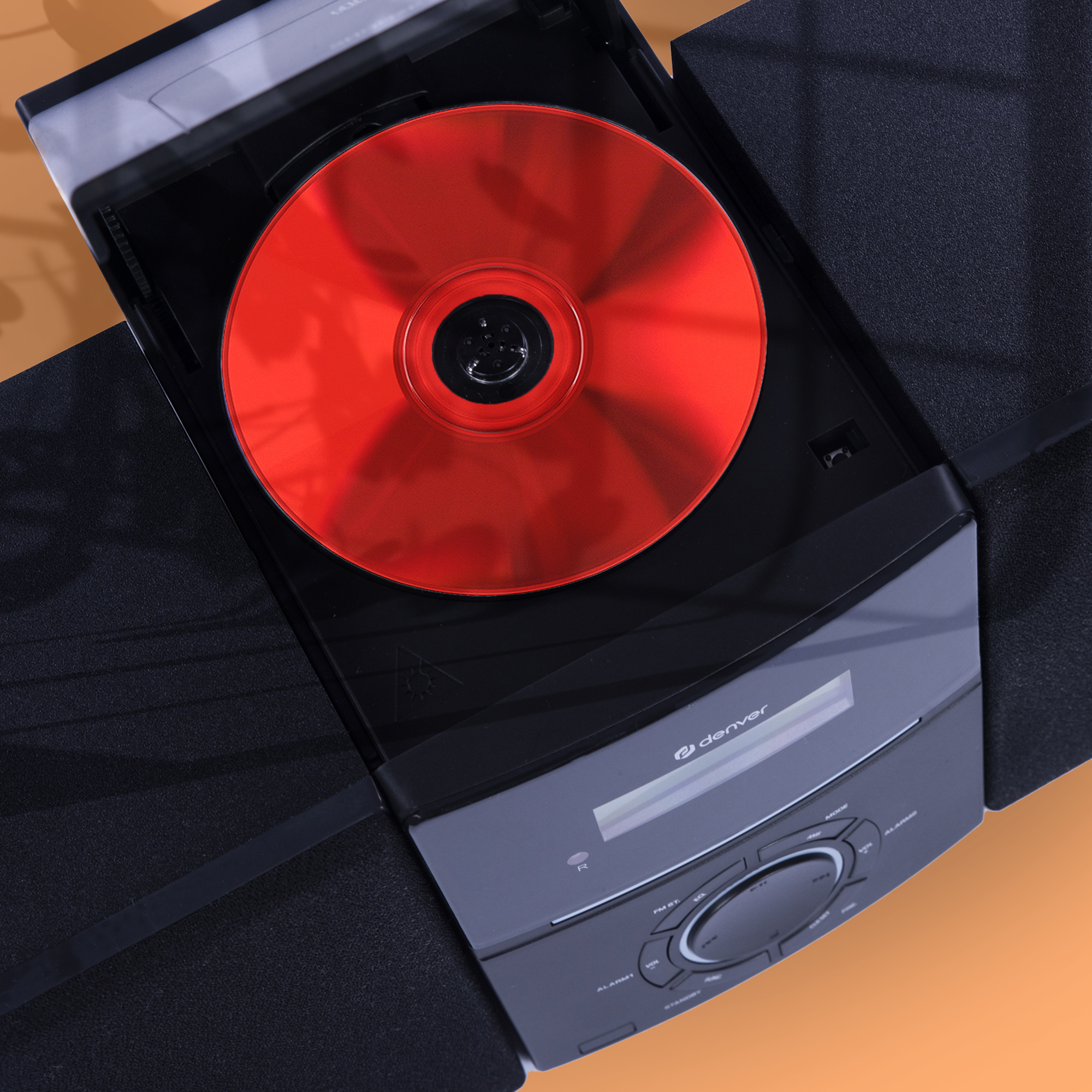Czarno-czerwony odtwarzacz CD z czerwoną płytą CD w środku. Urządzenie znajduje się na pomarańczowej powierzchni.