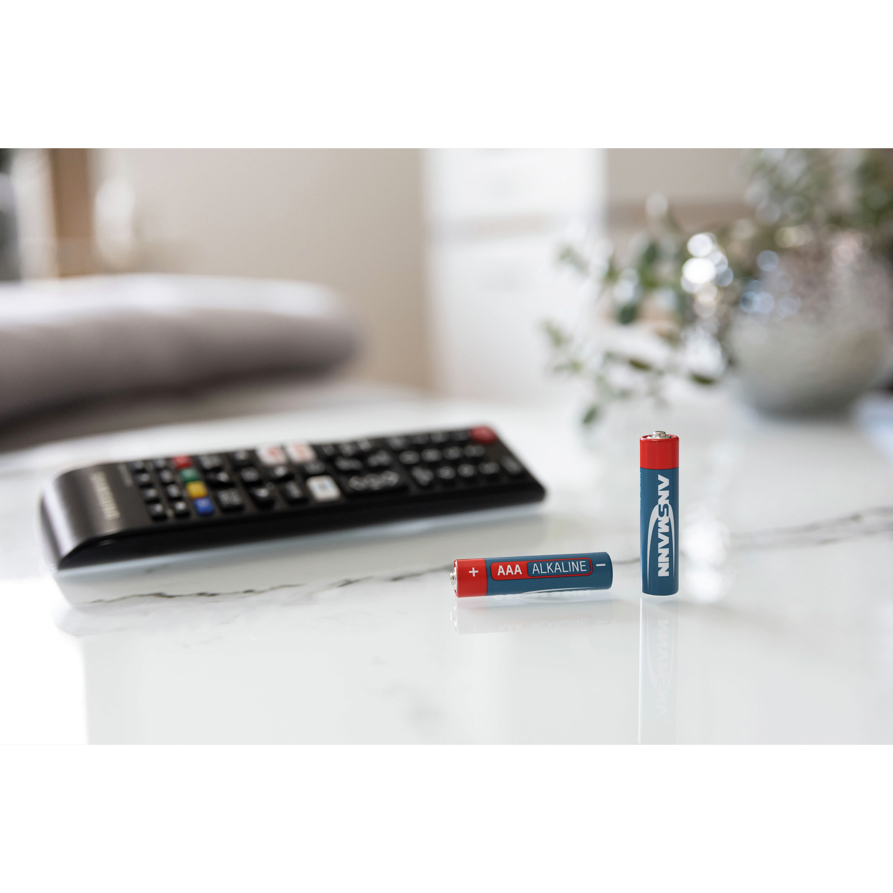 Zwei AAA-Alkalibatterien neben einer Fernbedienung auf einer Marmoroberfläche.