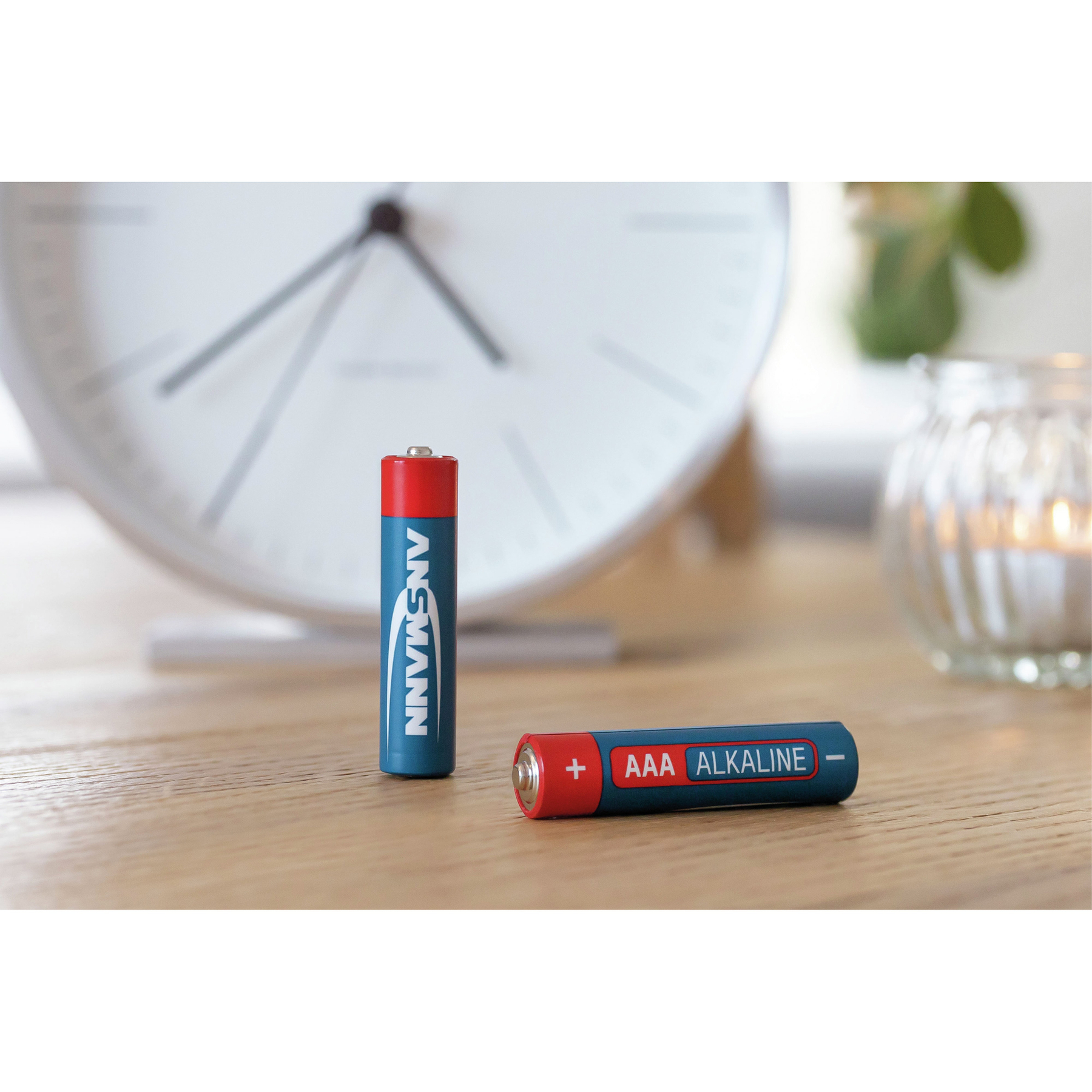 Zwei blau-rote AAA-Batterien auf einer Holzoberfläche neben einer Uhr.