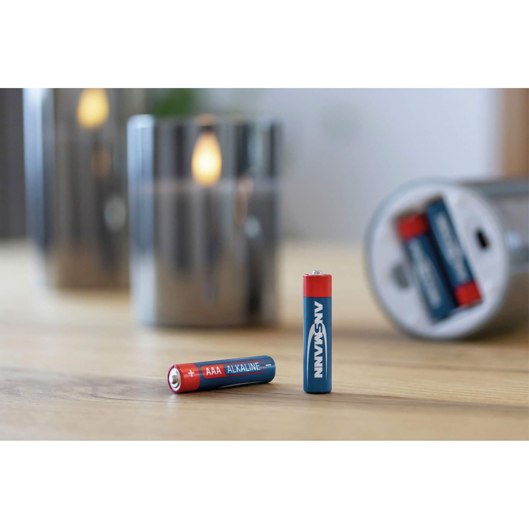 Zwei Batterien und silberne Kerzenhalter auf einem Holztisch. Eine Batterie ist blau und rot, die andere blau und silber.