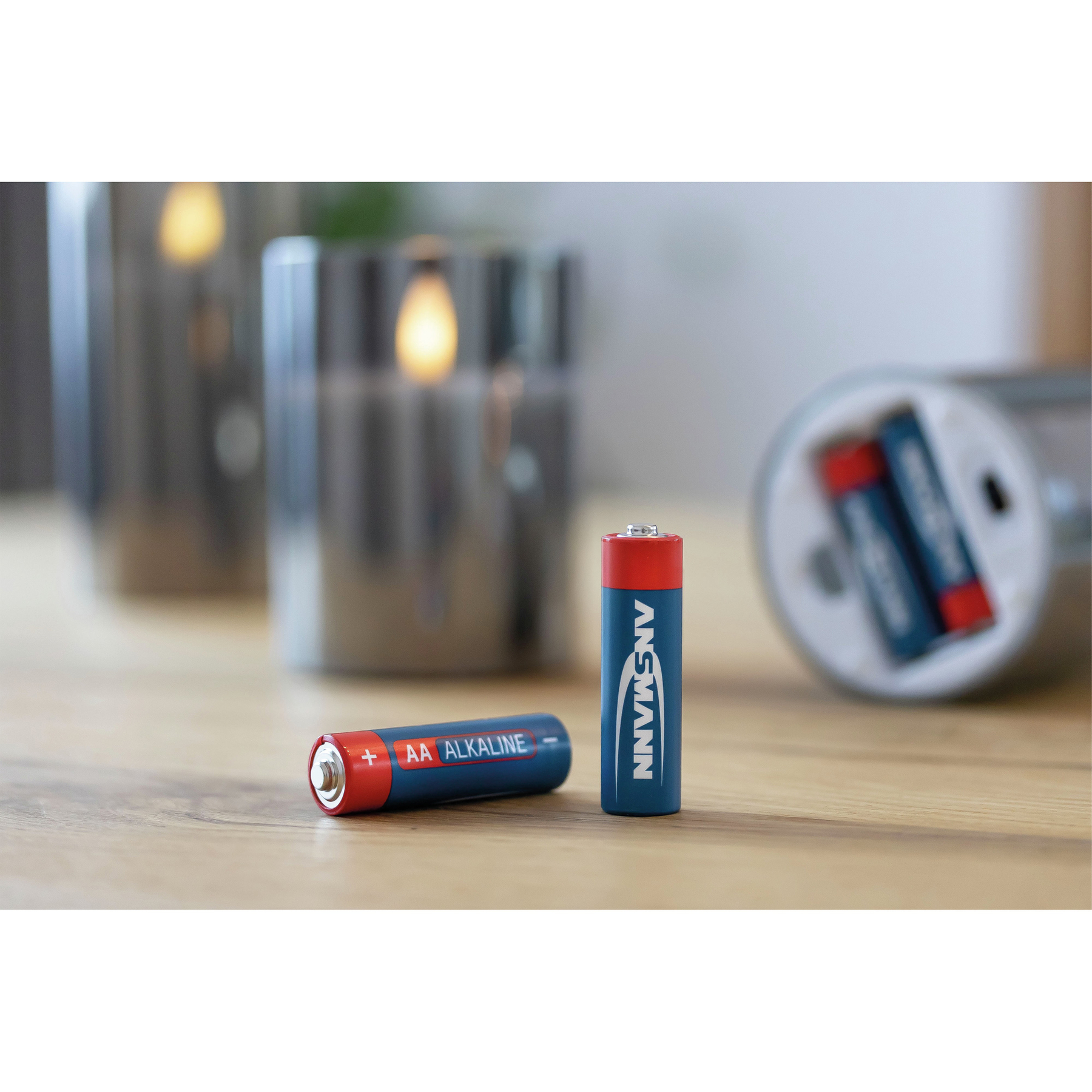 Dwie baterie AA. Jedna niebieska i jedna czerwona. Świecznik w tle. Drewniana powierzchnia.