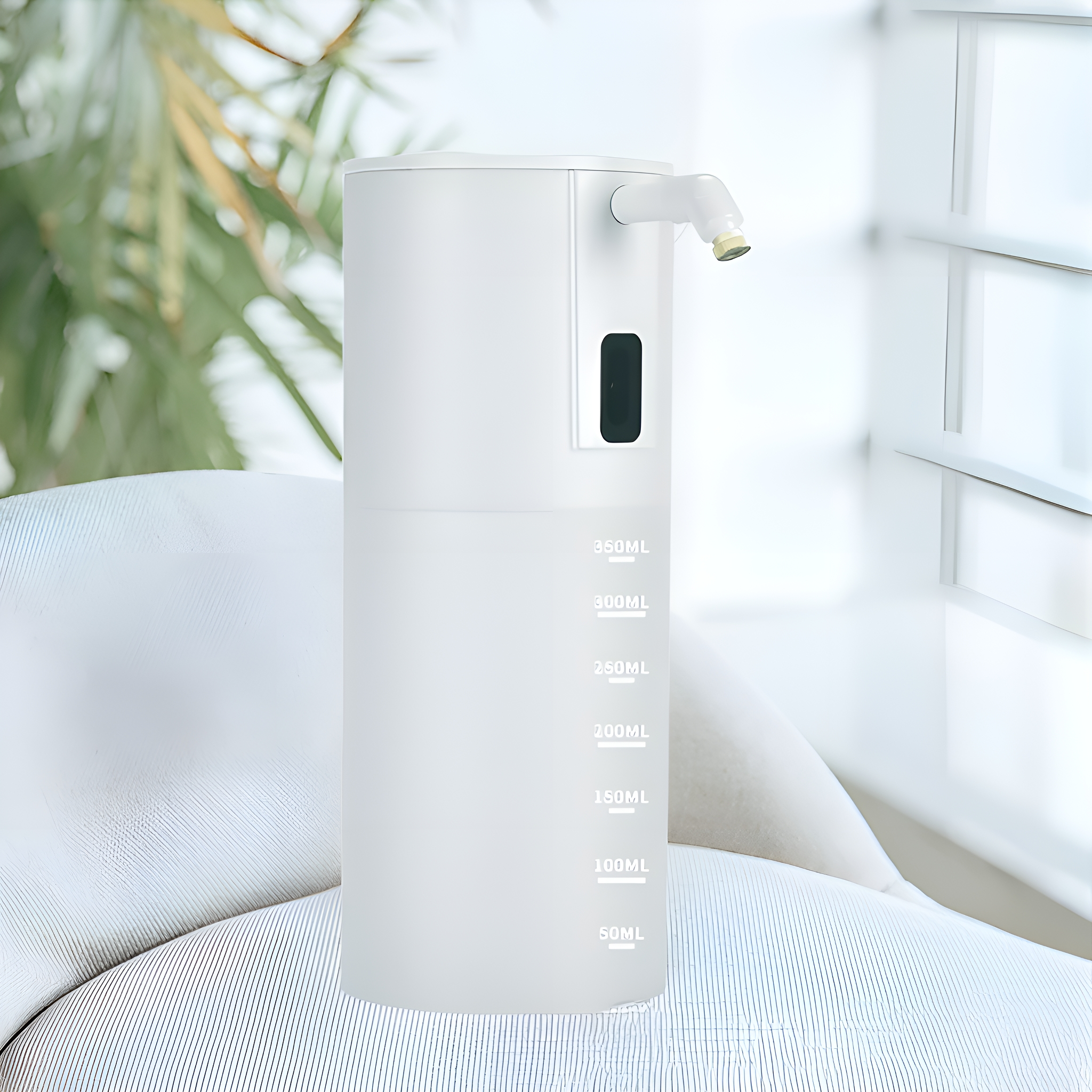 Weißer, automatischer Seifenspender mit Ausguss. Ein Fenster und eine Pflanze sind im Hintergrund.